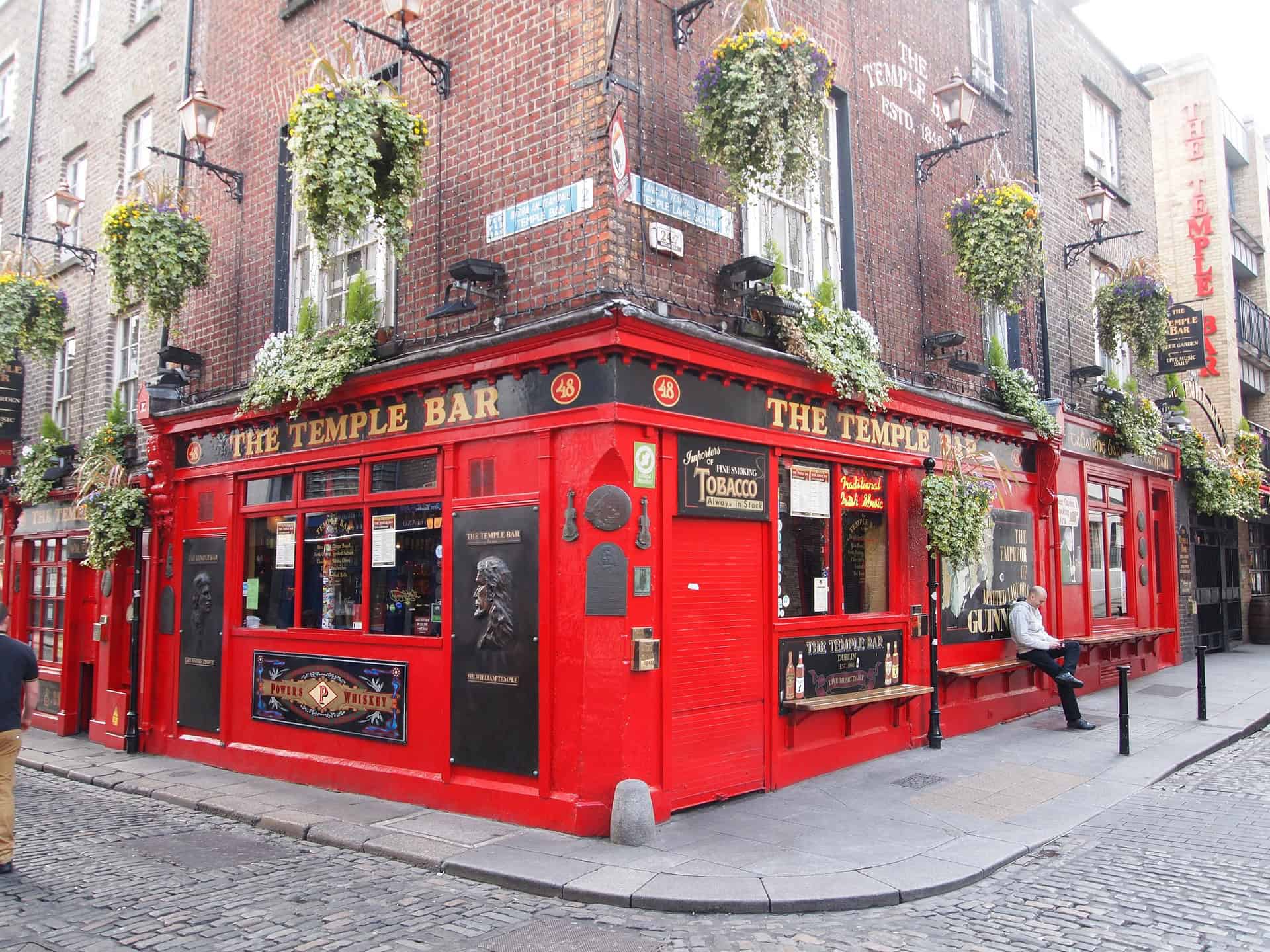 Bright red exterior of The Temple Bar, a famous Irish pub in Dublin, surrounded by hanging flower baskets.