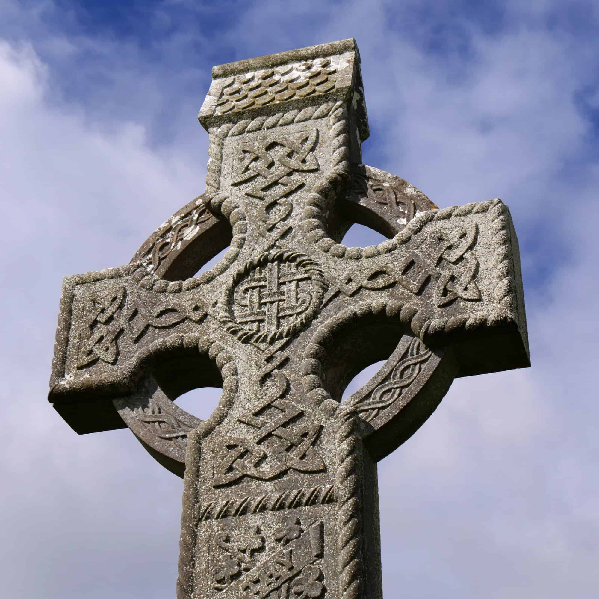 Intricate Irish Celtic cross monument against a cloudy sky.
