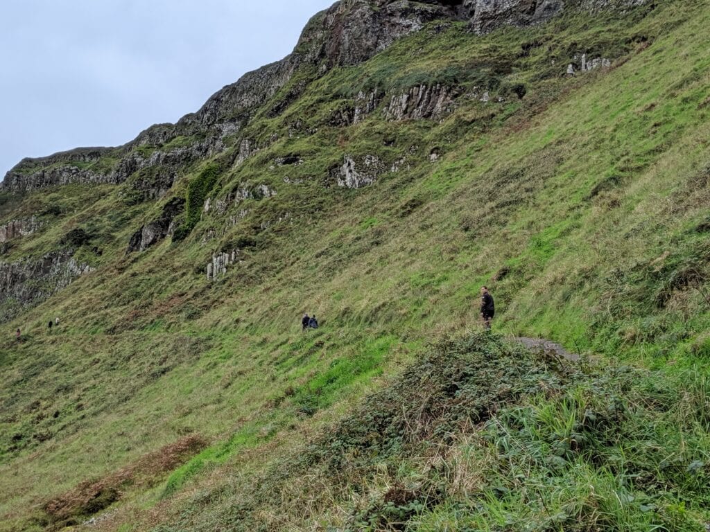 Cliffs of Moher with hikers on green hillside, Ireland.