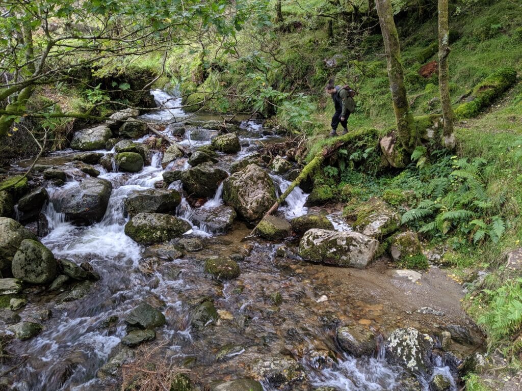 Irish forest stream with rocks and hiker in Connemara.