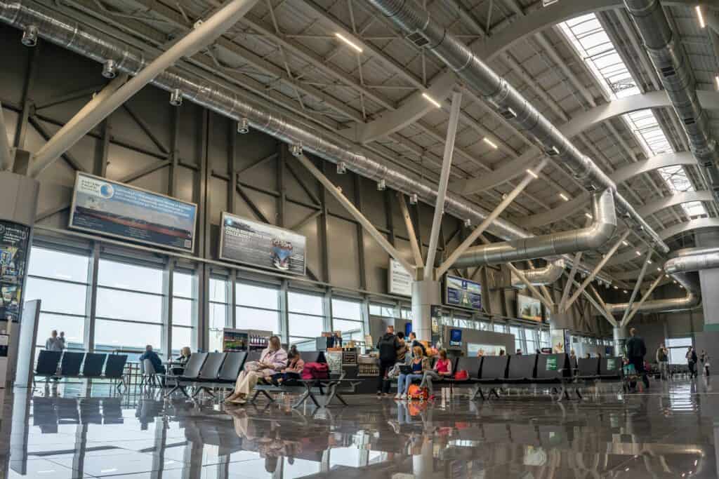Spacious airport terminal interior with passengers seated and walking, showcasing modern design and large windows.