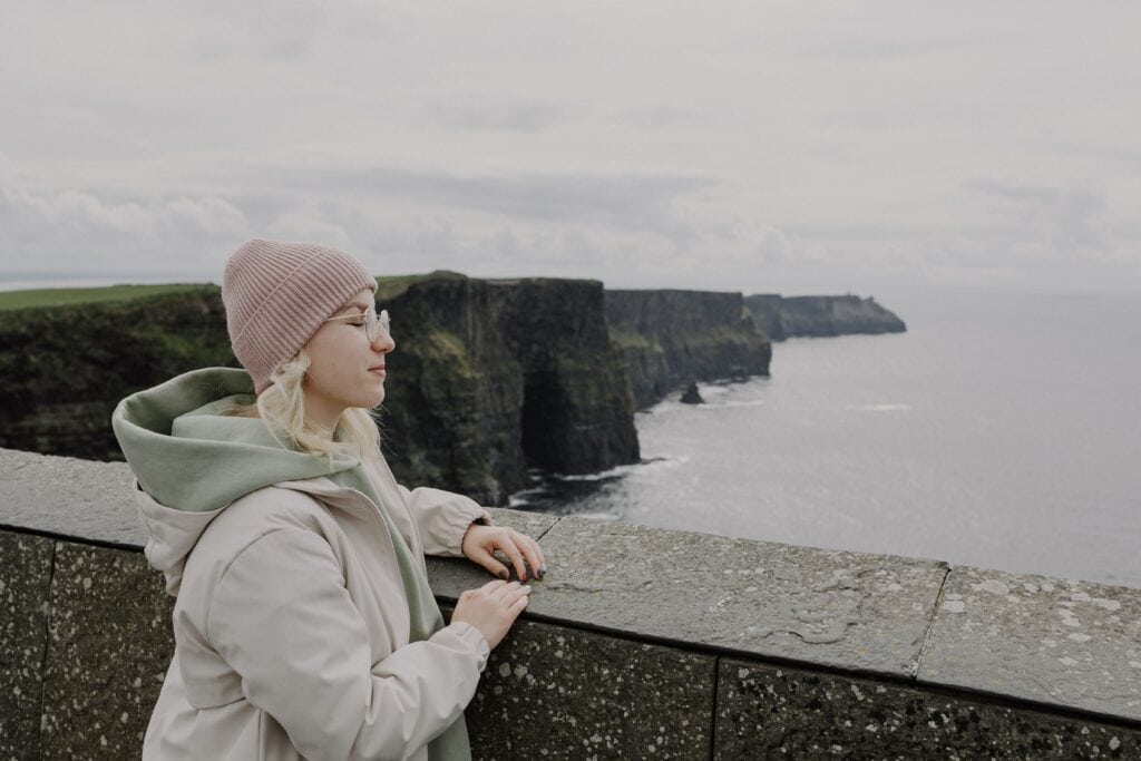 Woman in cozy attire admiring the famous Cliffs of Moher by the sea.