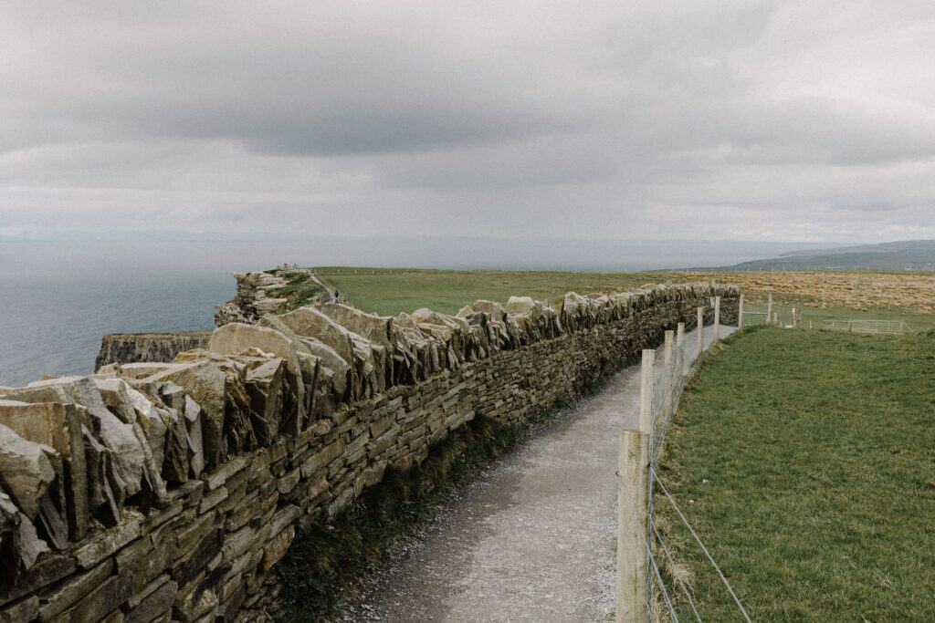 Explore the iconic Cliffs of Moher with this scenic view featuring a stone wall and ocean backdrop.
