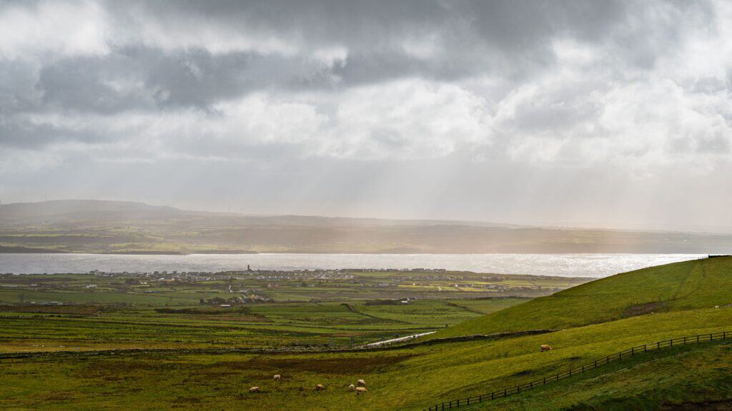 Dramatic clouds over green fields and distant water in Burren, Ireland.