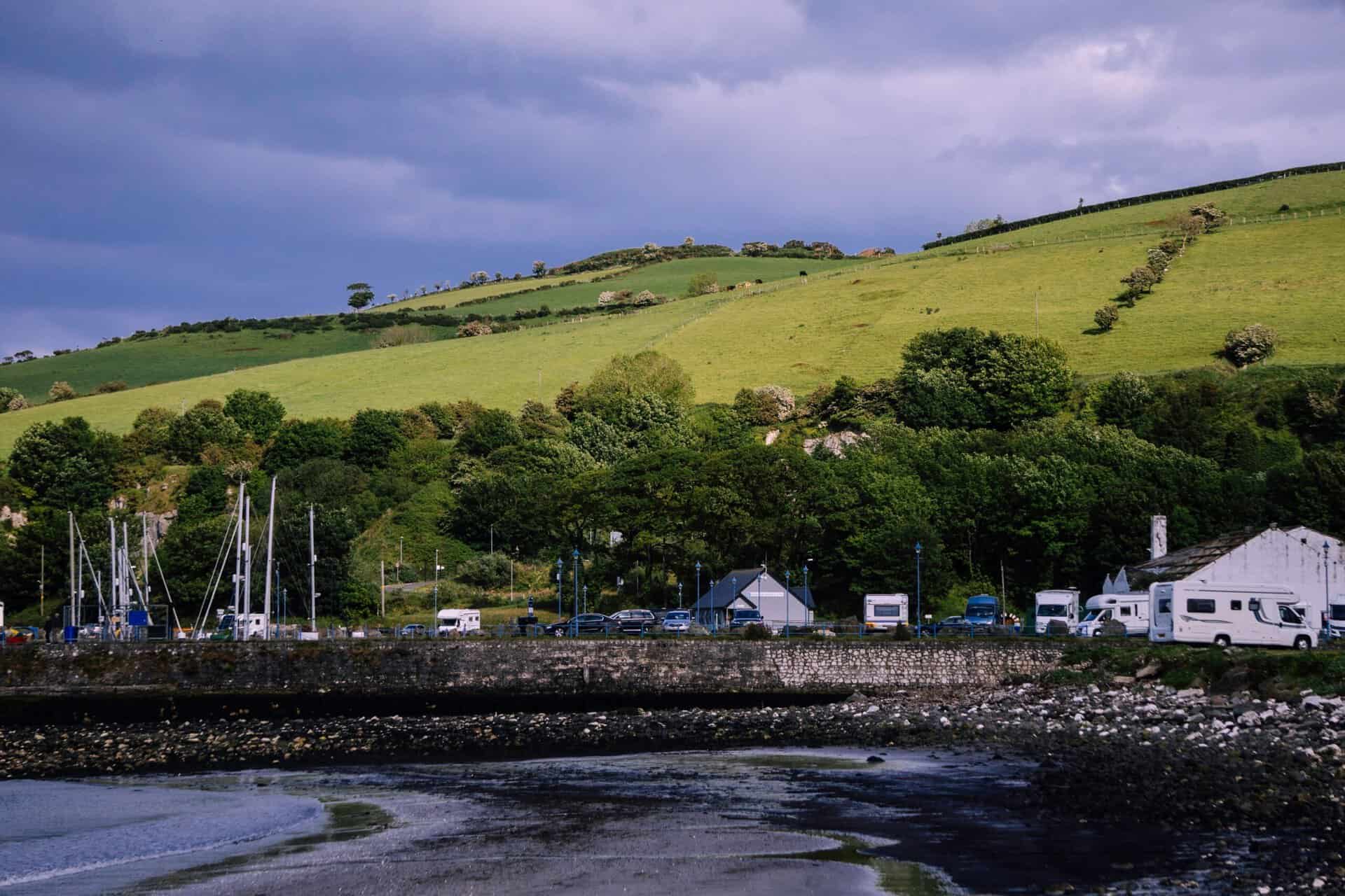 Irish coast with boats, green hills, and cloudy sky.
