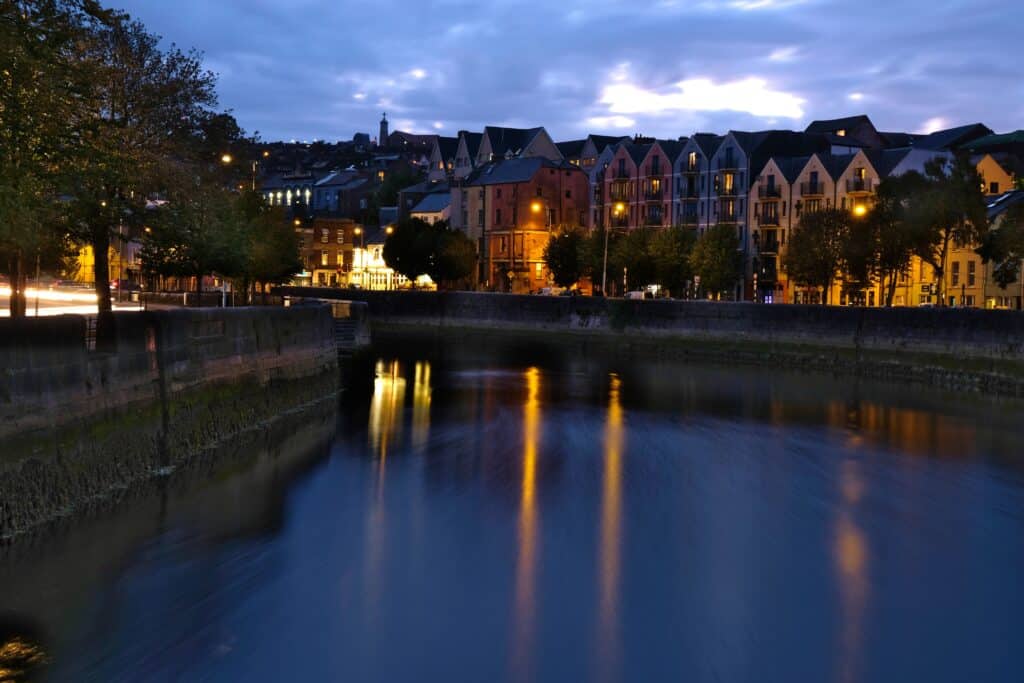 River Lee flowing through Cork City at dusk, with colorful buildings and a.