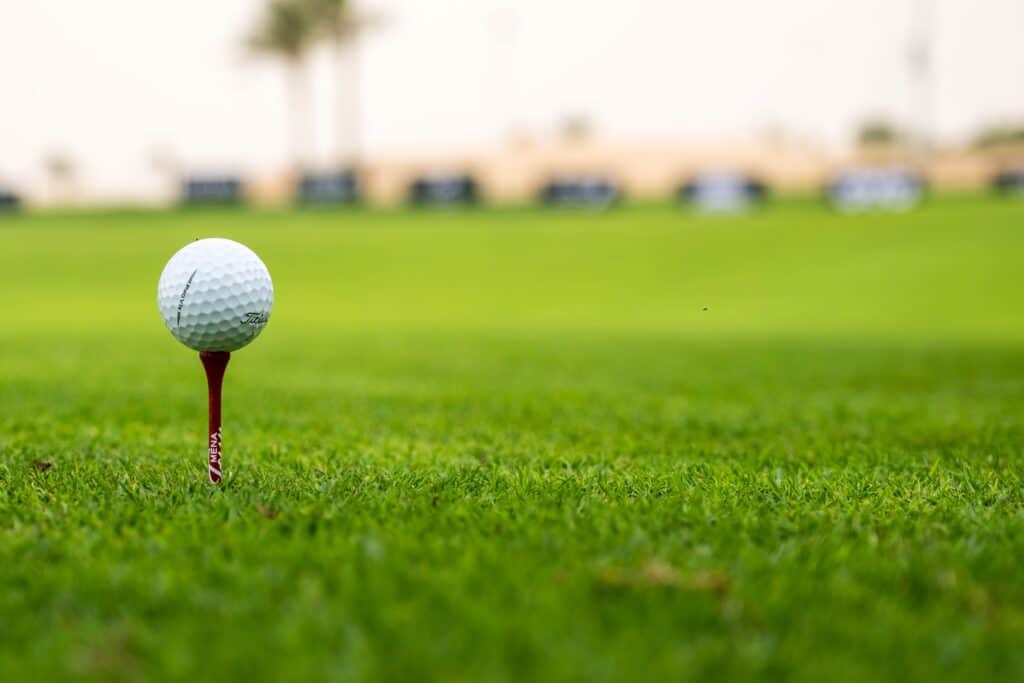 A close-up view of a golf ball on a tee set on a lush green golf course, perfect for sports enthusiasts.