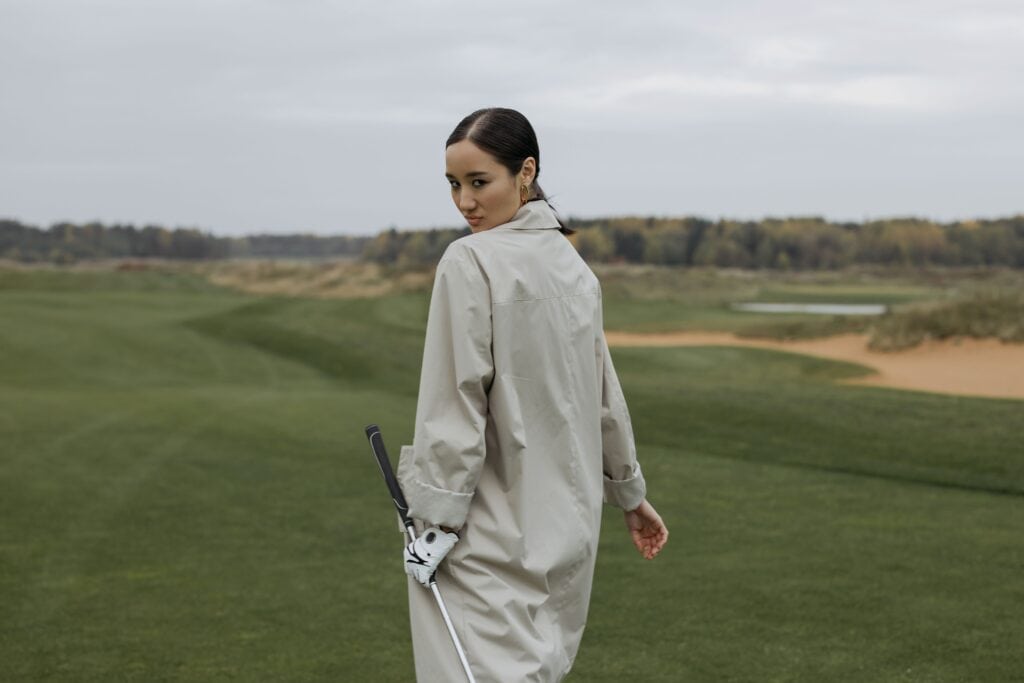 Woman in beige coat on Irish golf course with golf club.