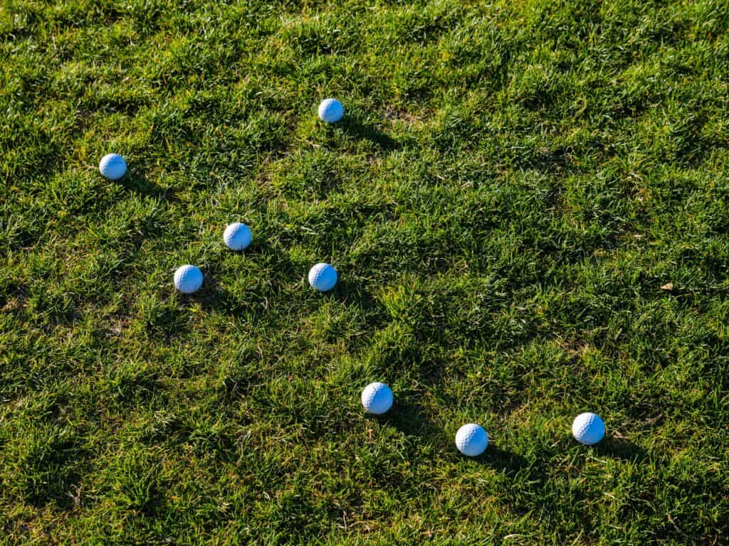 Multiple golf balls scattered on a lush green grass field under bright daylight.