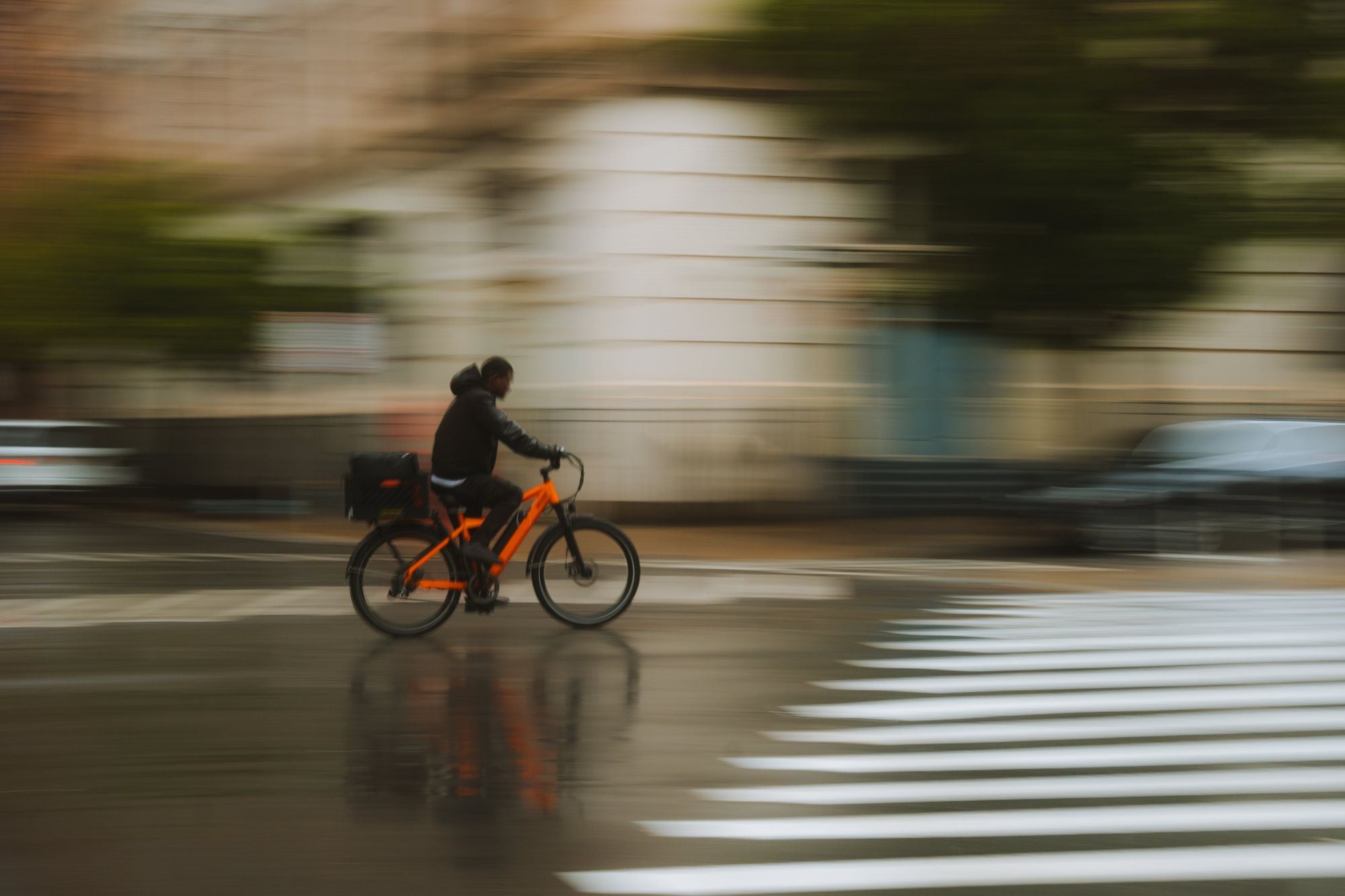 A fast-moving cyclist rides through rainy city streets, capturing motion and energy.