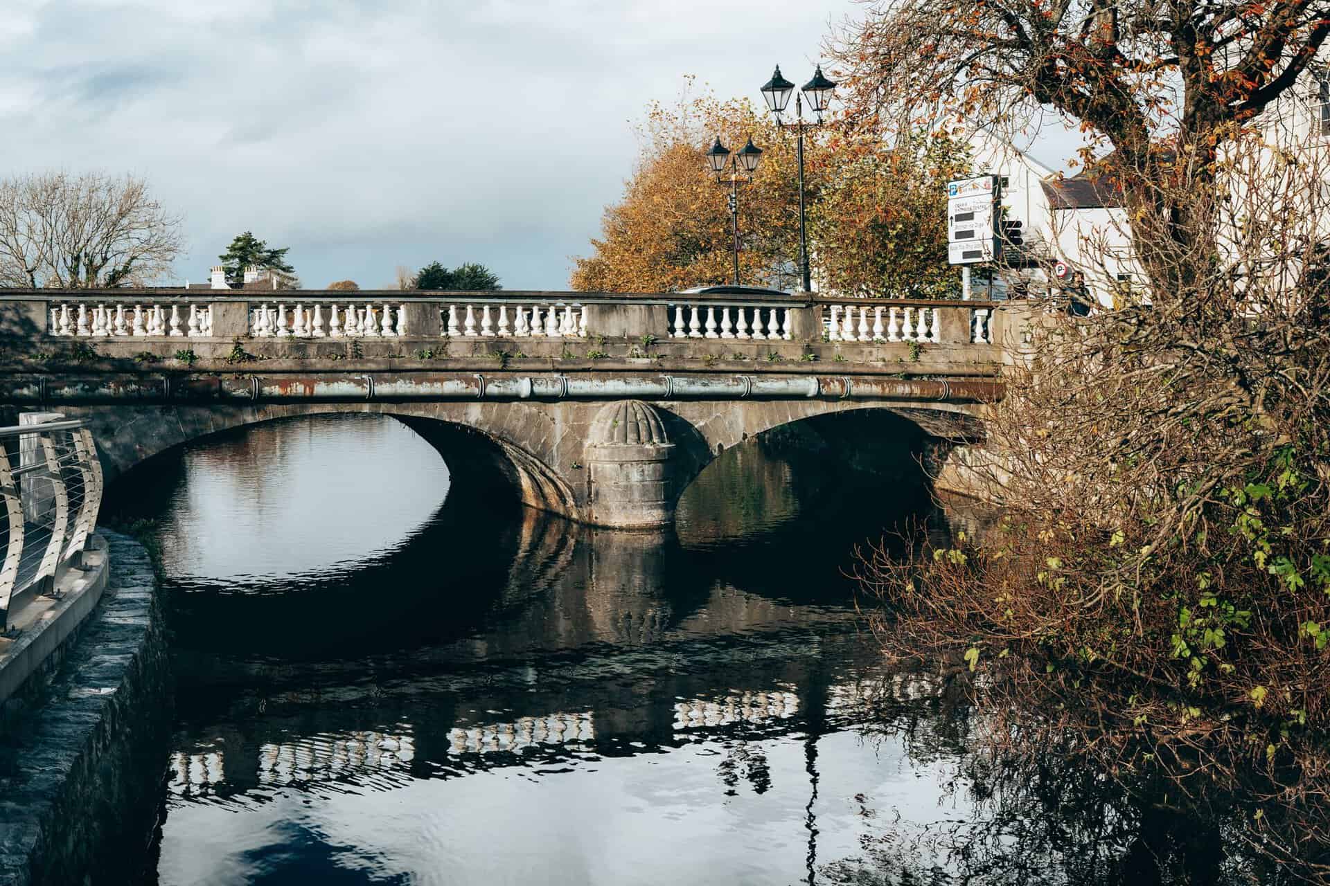 A scenic autumn view of a historic stone bridge over a calm river in Galway, Ireland.