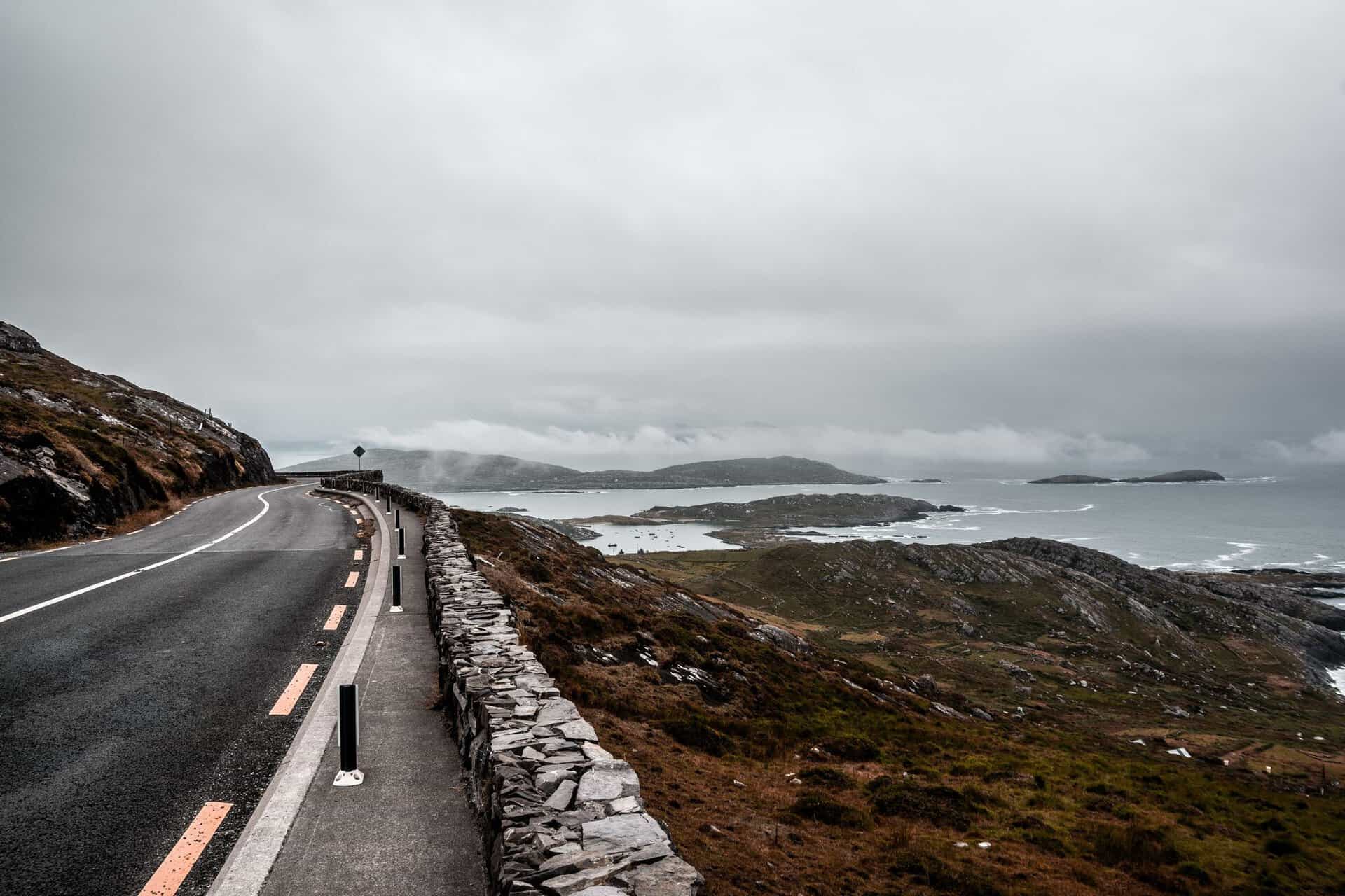A winding road along a rugged coastline with dramatic ocean views under a cloudy sky.