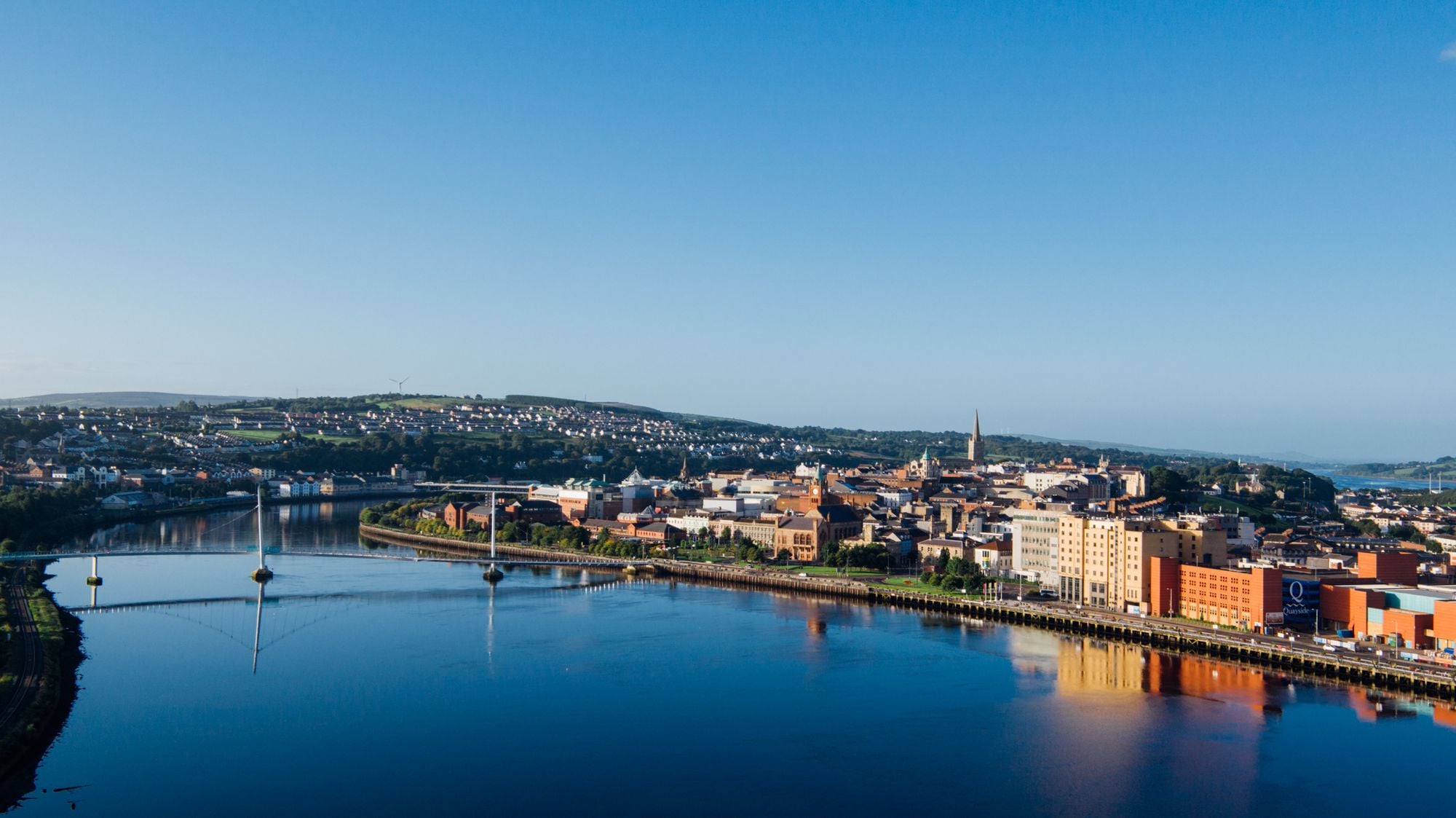 Aerial shot of Derry city and Peace Bridge over River Foyle at sunrise.