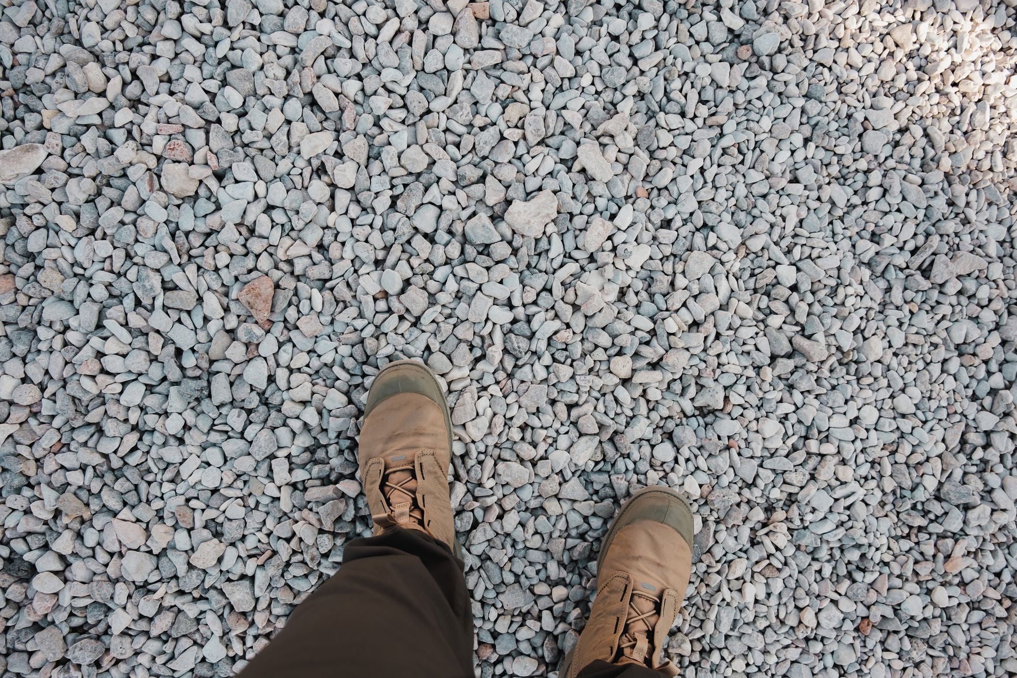 Aerial shot of rugged boots standing on a field of gravel stones, emphasizing outdoor adventure.