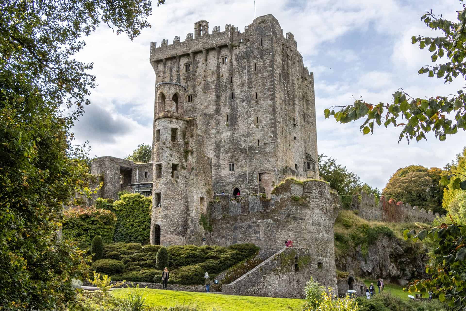 Historic Blarney Castle set against a backdrop of vibrant greenery and a partly cloudy sky.