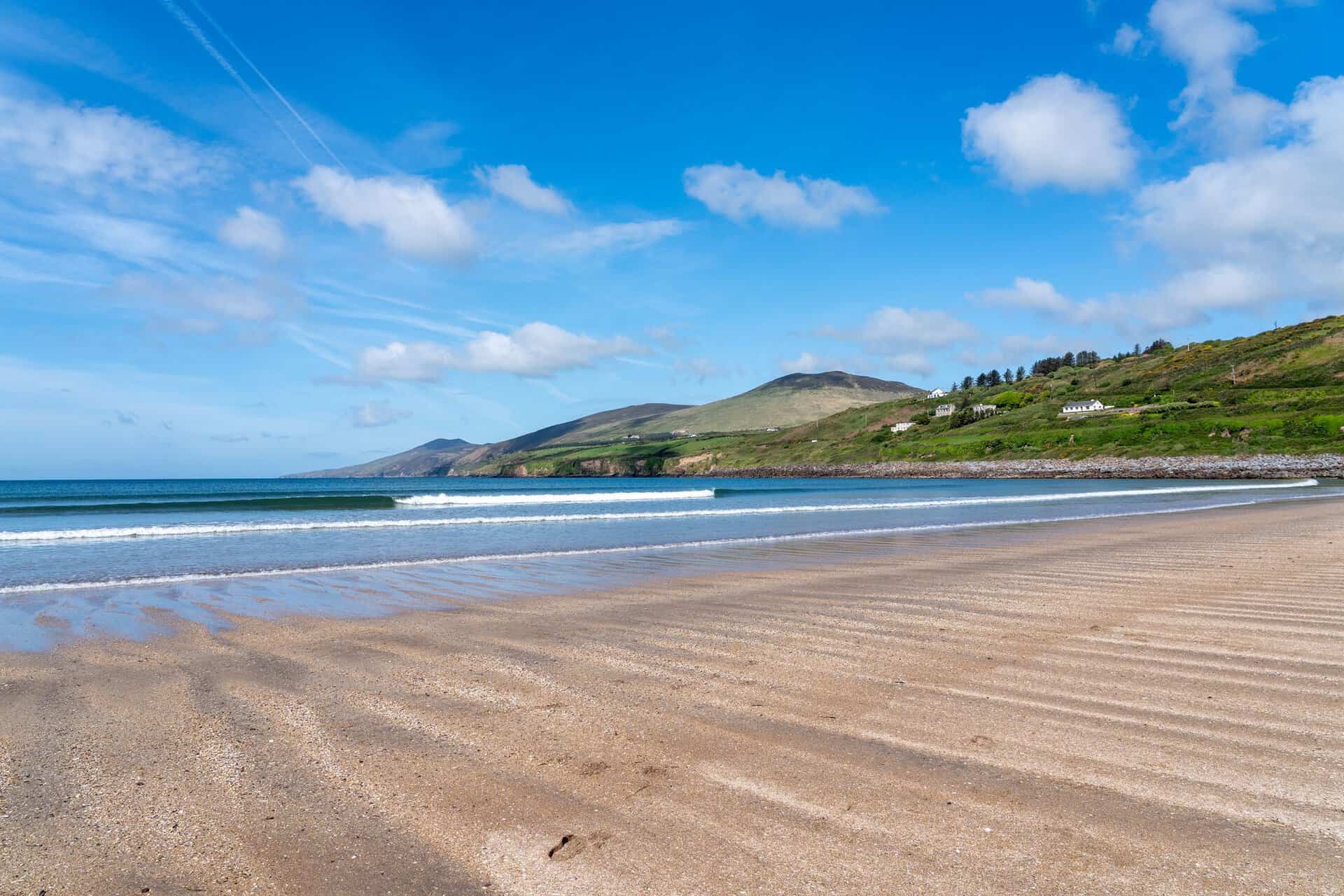 Tranquil beach with rolling waves and lush hills on Dingle Peninsula, Ireland.