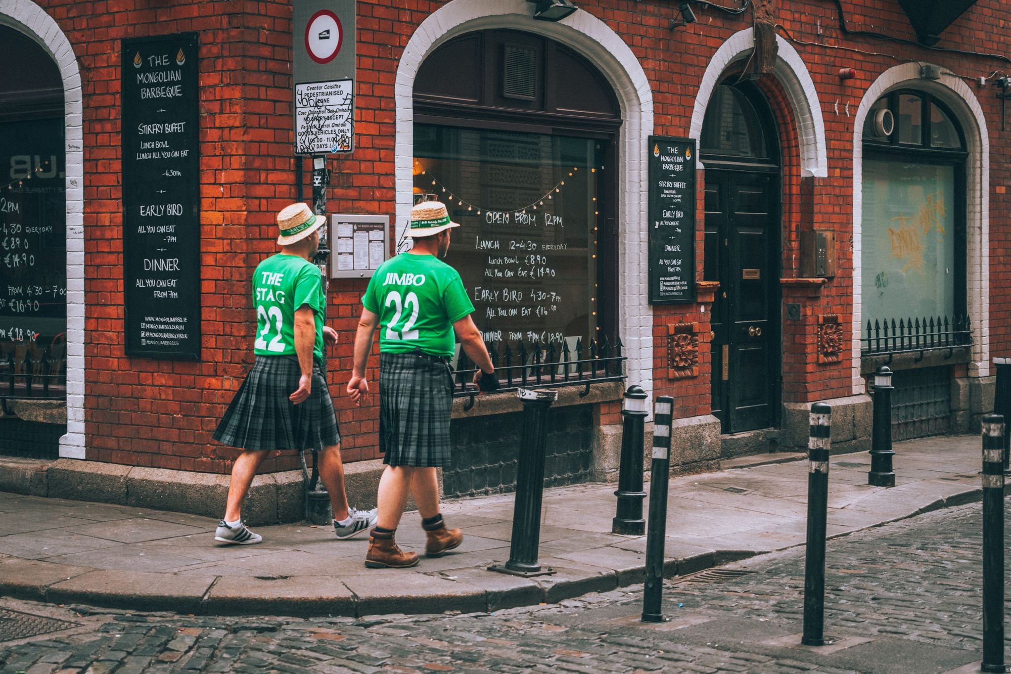 Two men in green jerseys and kilts walking past a restaurant in Dublin, Ireland.