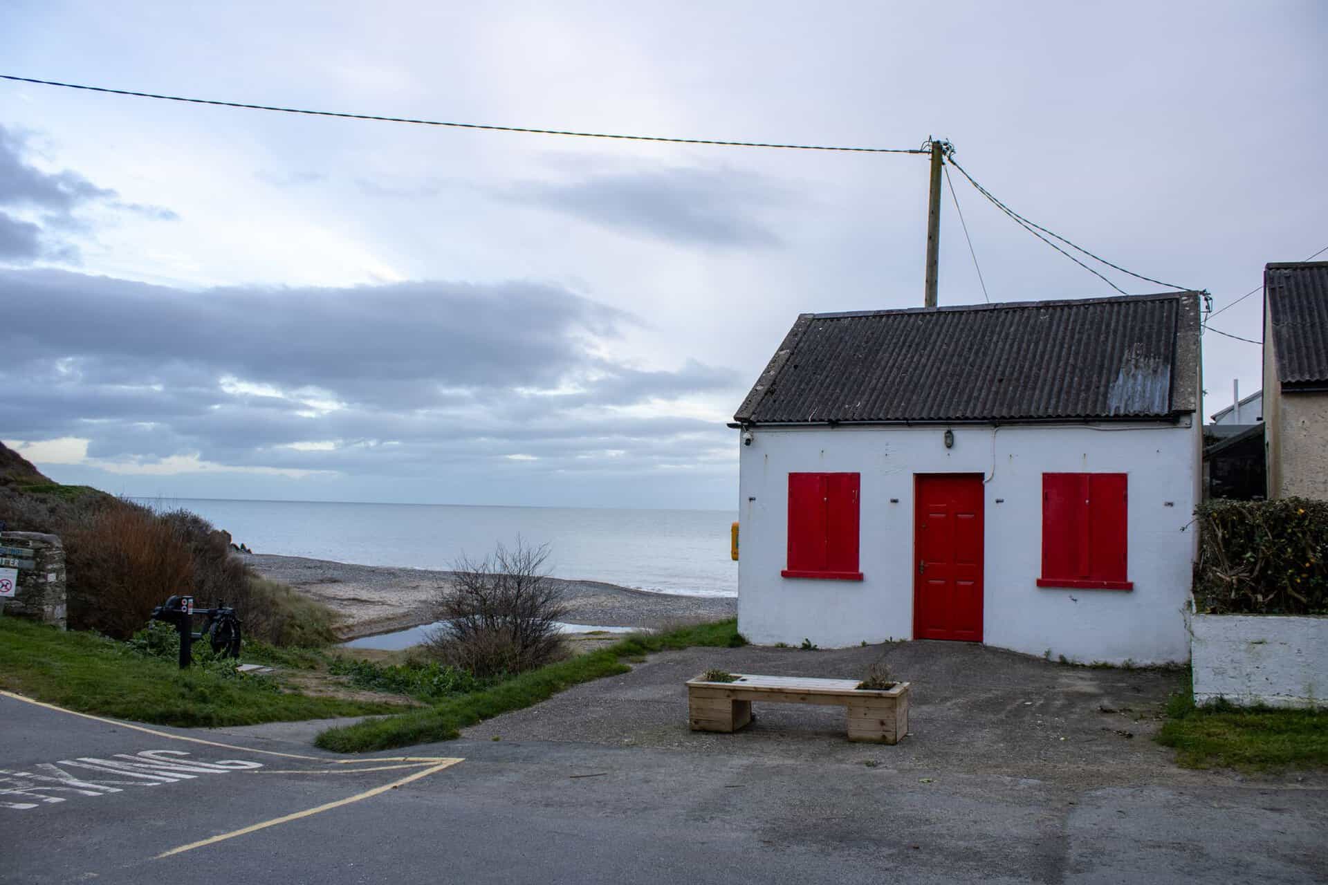 White cottage with red shutters by a beach in Ballymoney, Ireland.