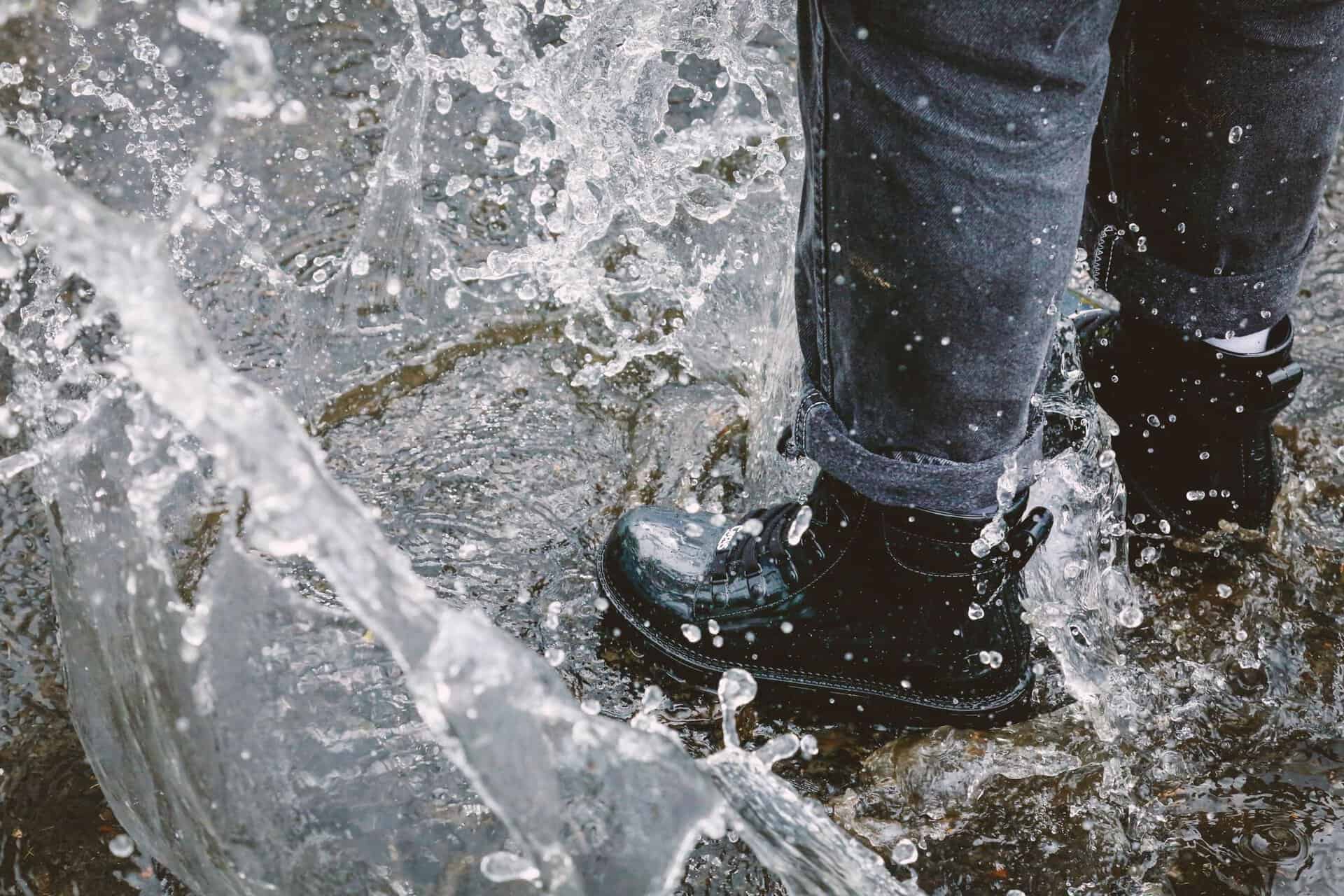 A close-up of a person stomping in water with waterproof boots, capturing a playful splash.