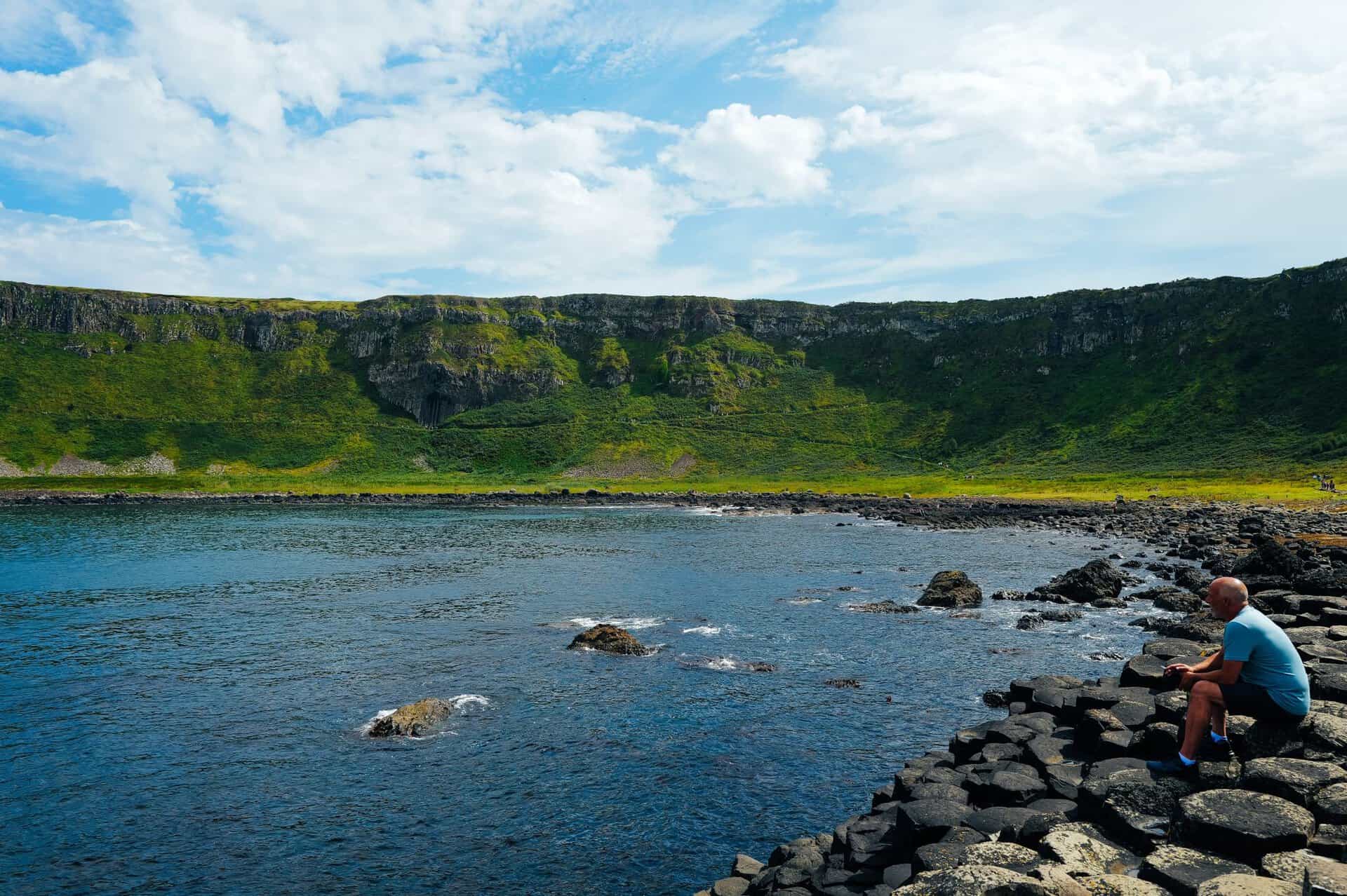 A man sits on the rocky coast of Giant's Causeway, enjoying the scenic view.