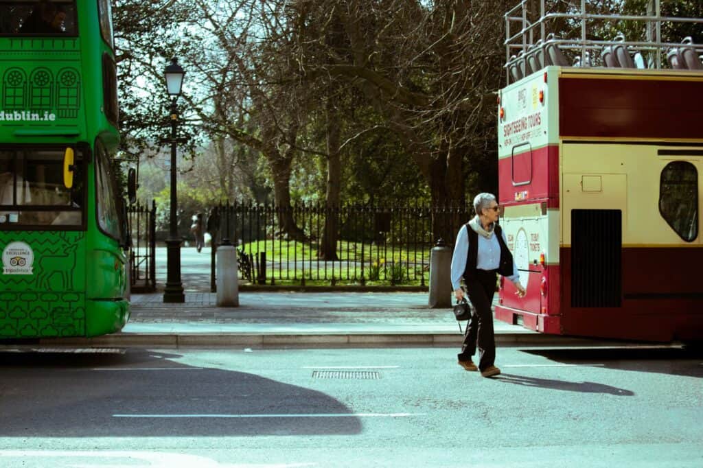 A man walks between two tour buses on a sunny day in Dublin, Ireland, highlighting urban travel vibes.