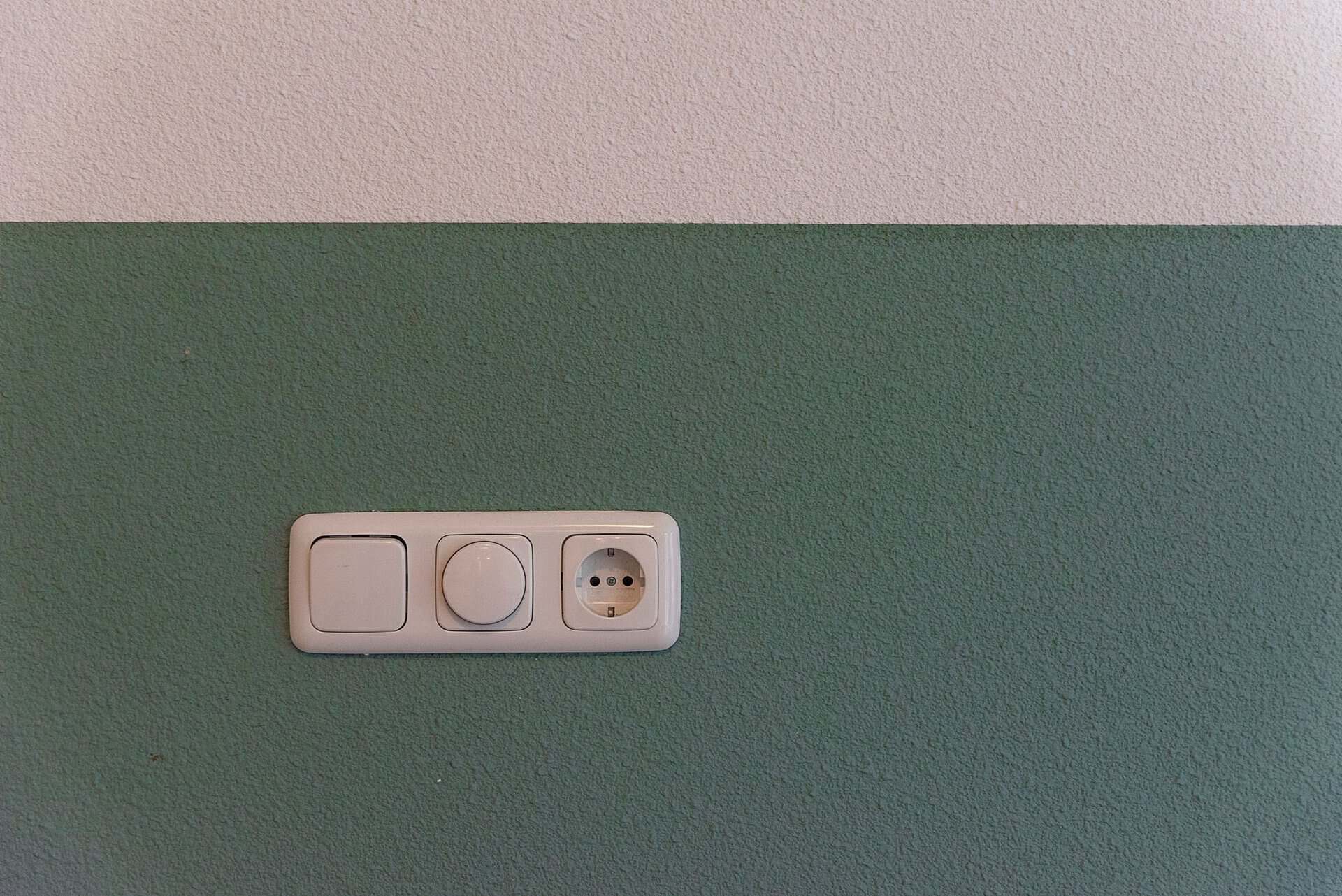 Close-up of a power outlet and switch on a textured green wall indoors.
