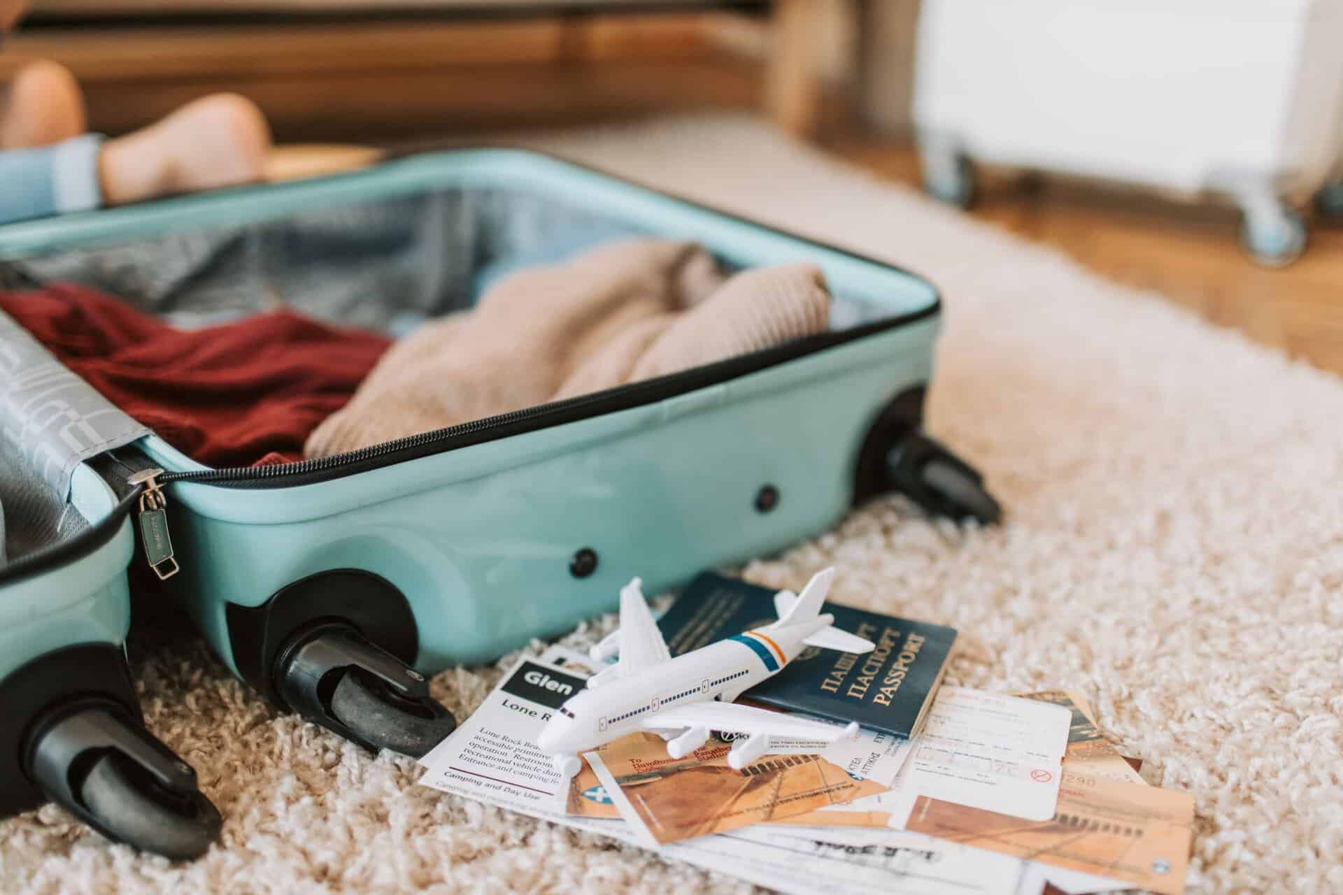 Open suitcase beside a passport, travel documents and a model aeroplane