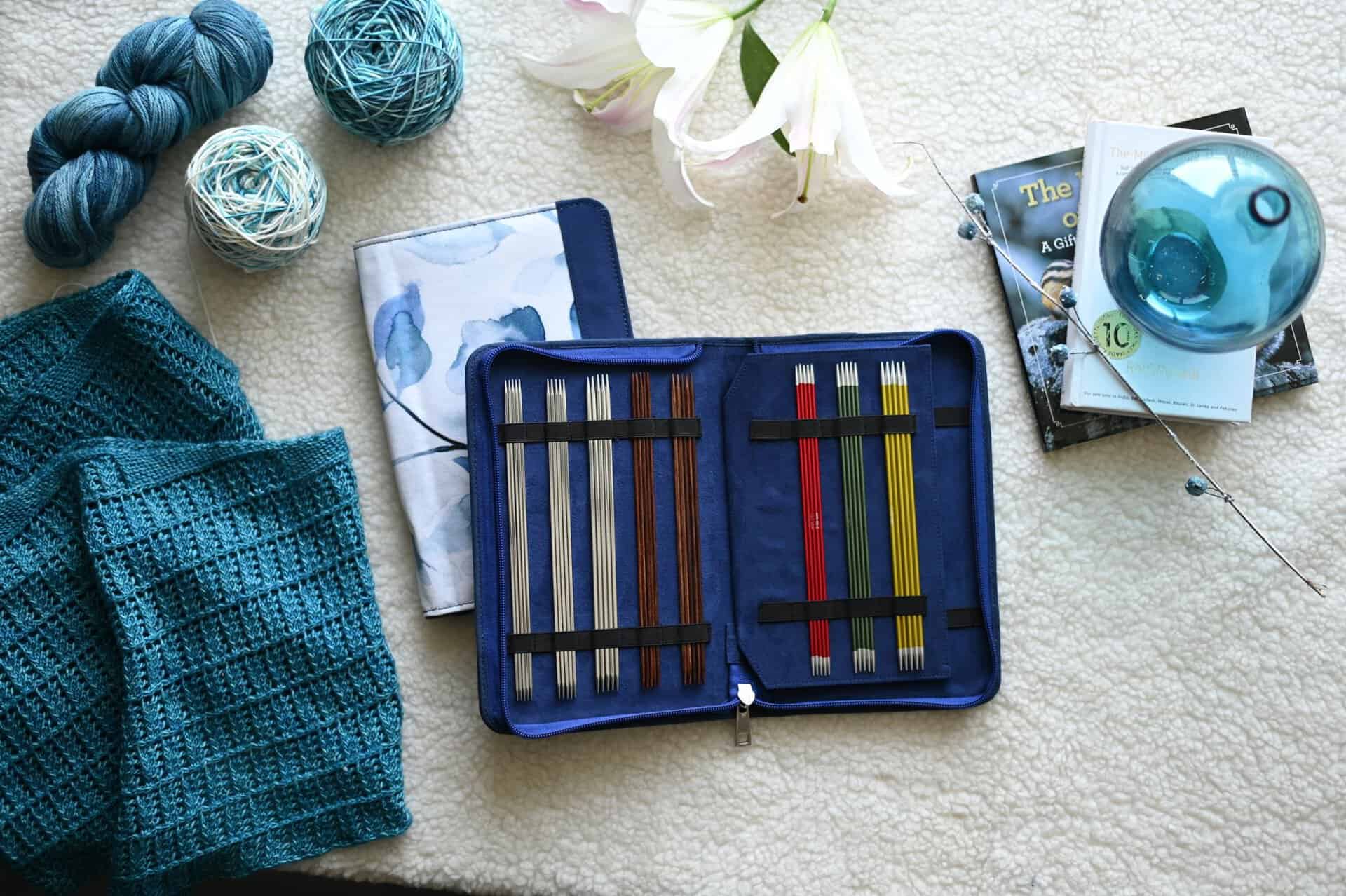 Flatlay of a knitting kit with colorful needles, yarn rolls, and fabric. Perfect for craft enthusiasts.