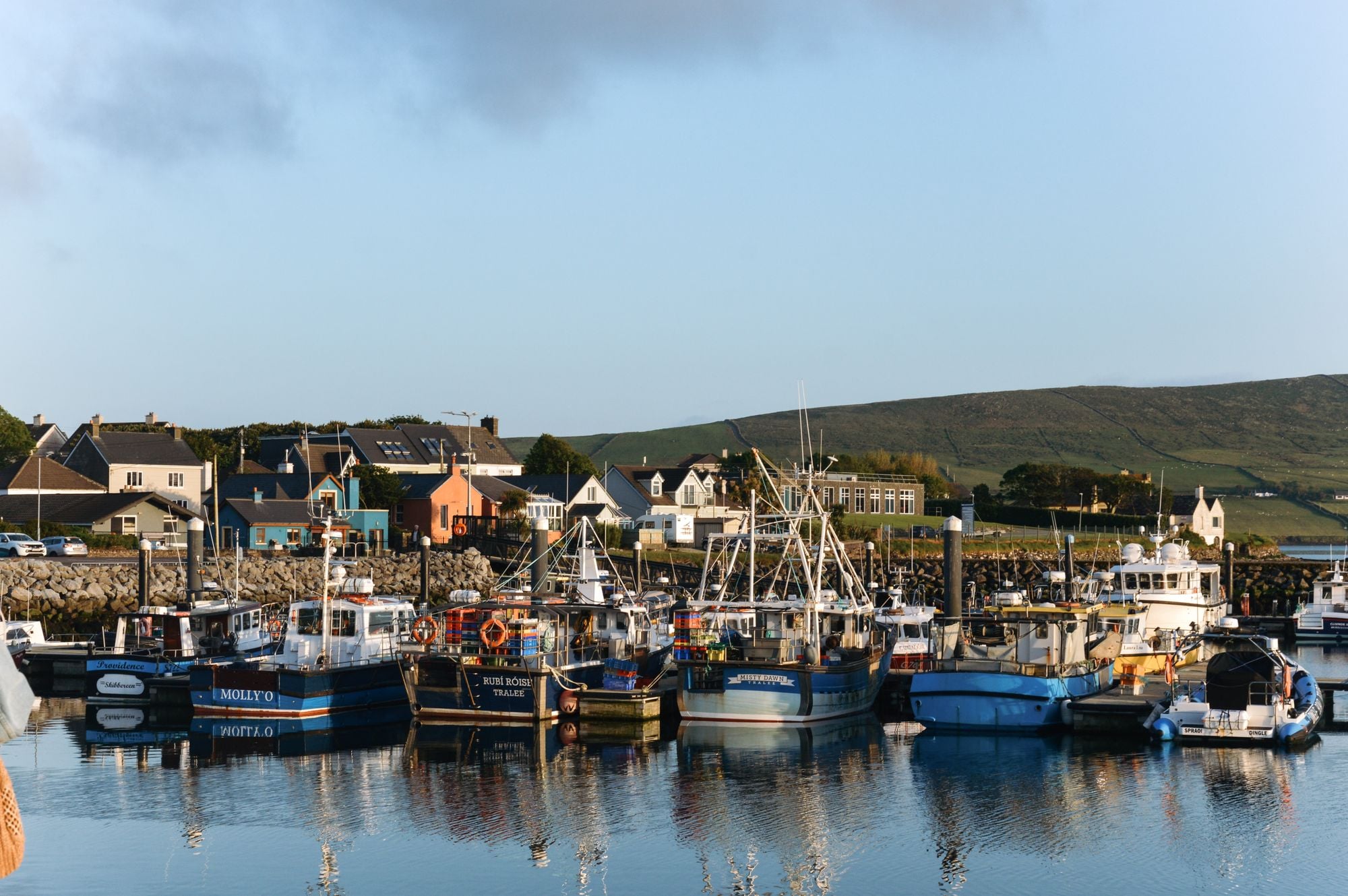 Picturesque harbor in Dingle, Ireland with fishing boats docked and colorful houses in the background.