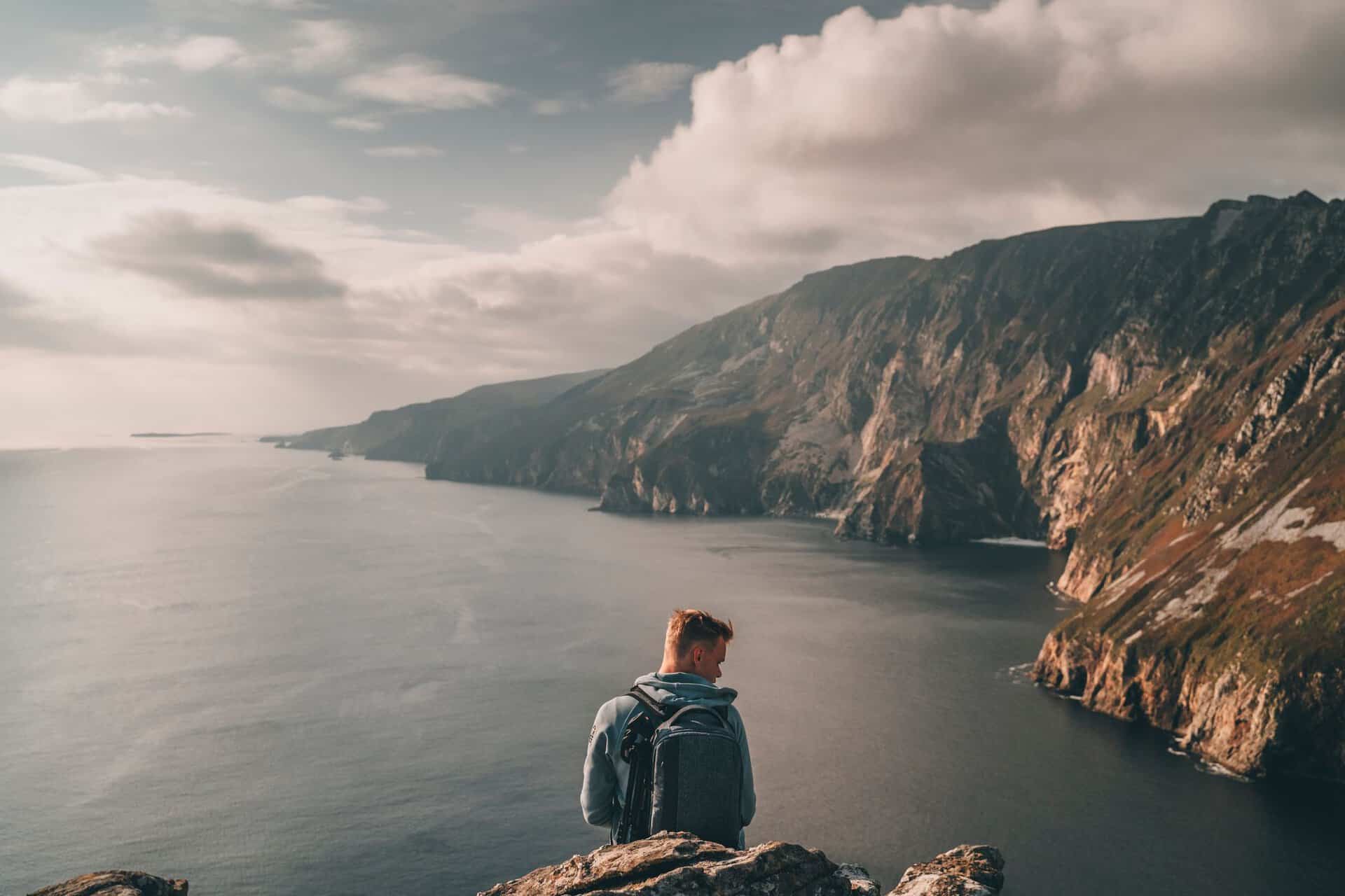 Traveler enjoying the stunning coastal cliffs of Ireland under a cloudy sky.
