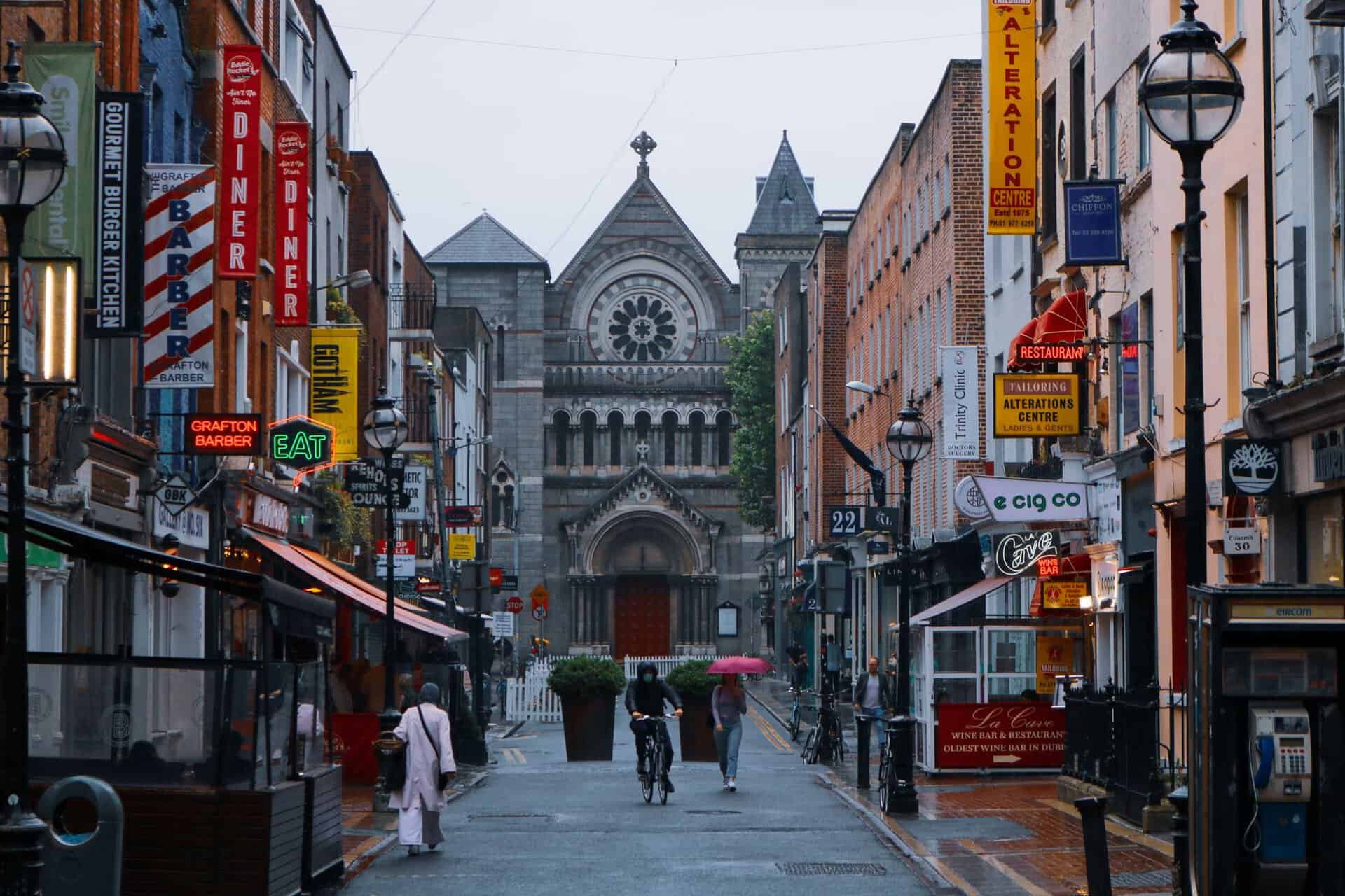 View of a vibrant street in Dublin with St. Ann's Church and shops. People walking in the rain.