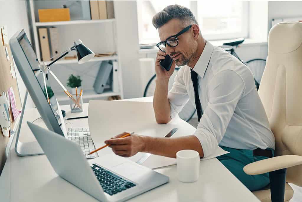 A person is talking with someone on the phone while working on his computer