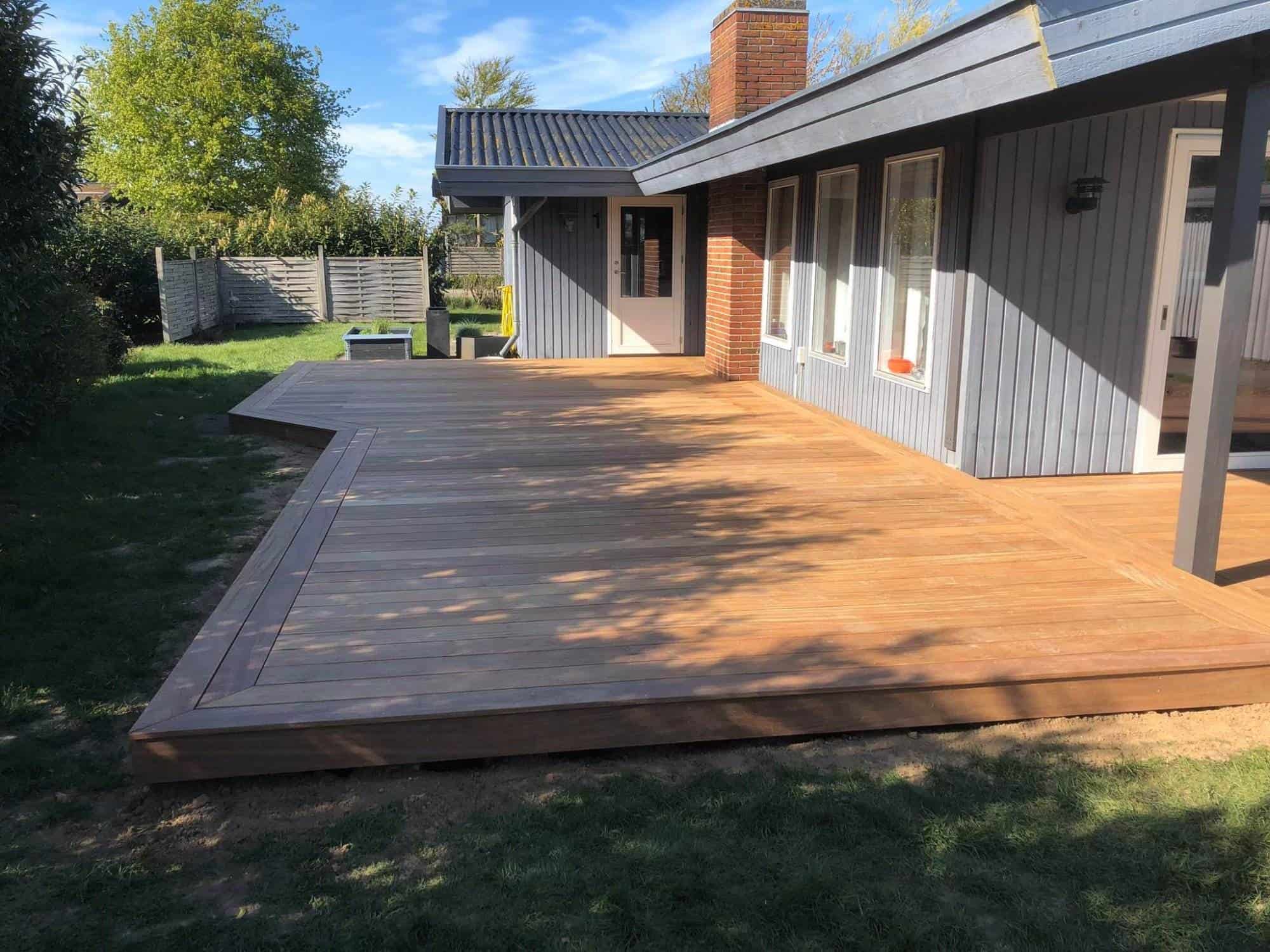 Udendørs trædæk foran hus med terrasse og have.
