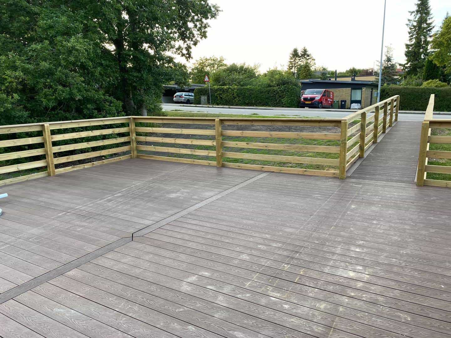 Træterrasse med trægelænder og udsigt over grønne områder.