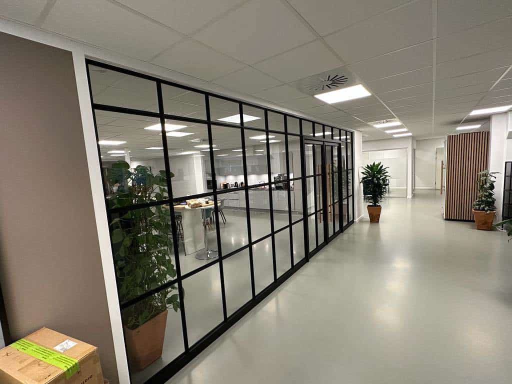 Kontor med store glasvægge og indendørs planter.