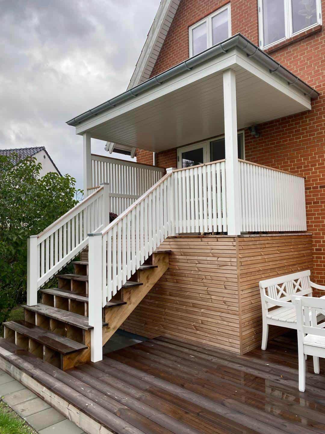 Trappe og veranda i træ med hvidt gelænder, perfekt til udendørs ophold og adgang.