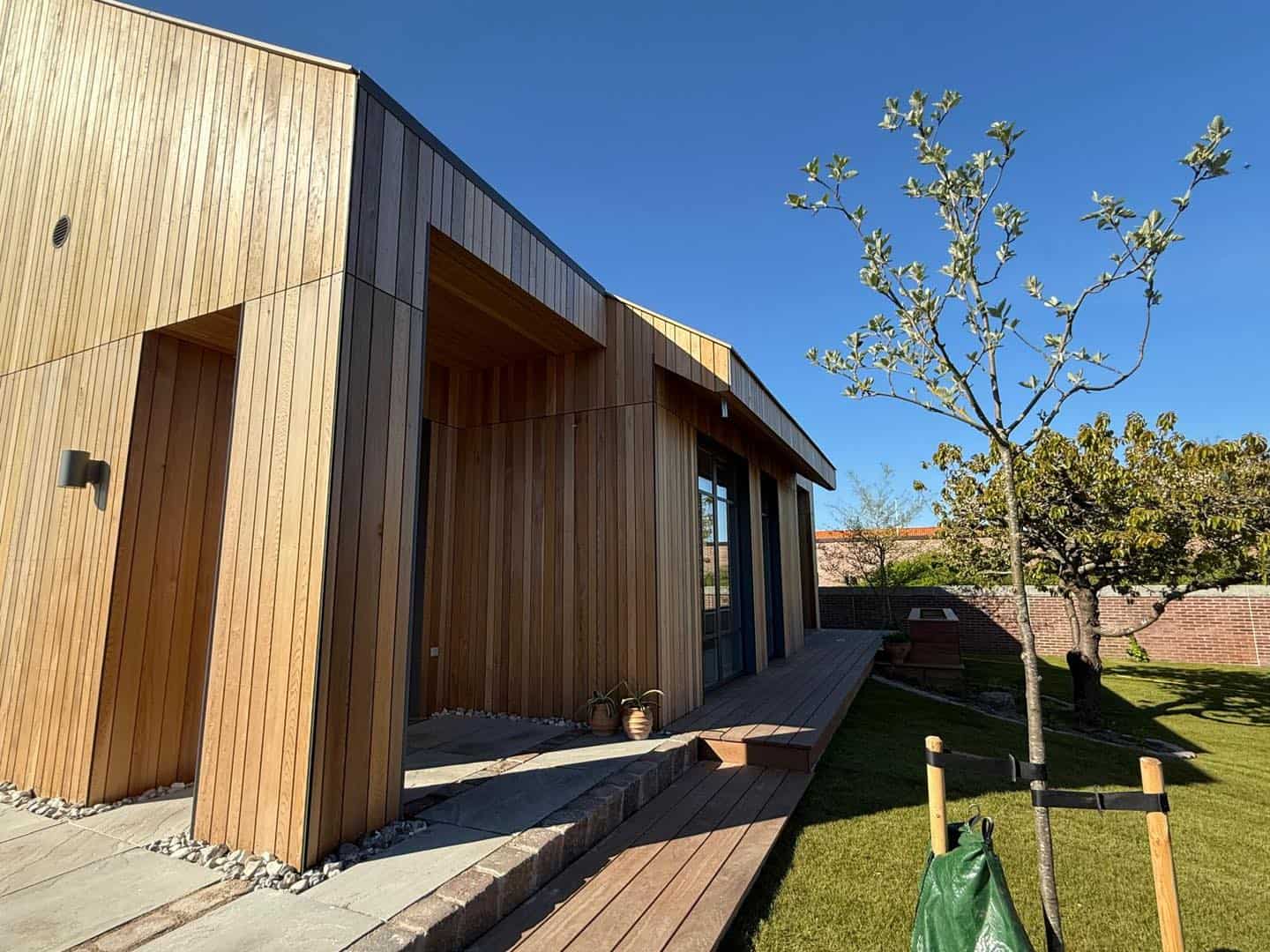 Træhus med moderne facade og store vinduer i et grønt område.