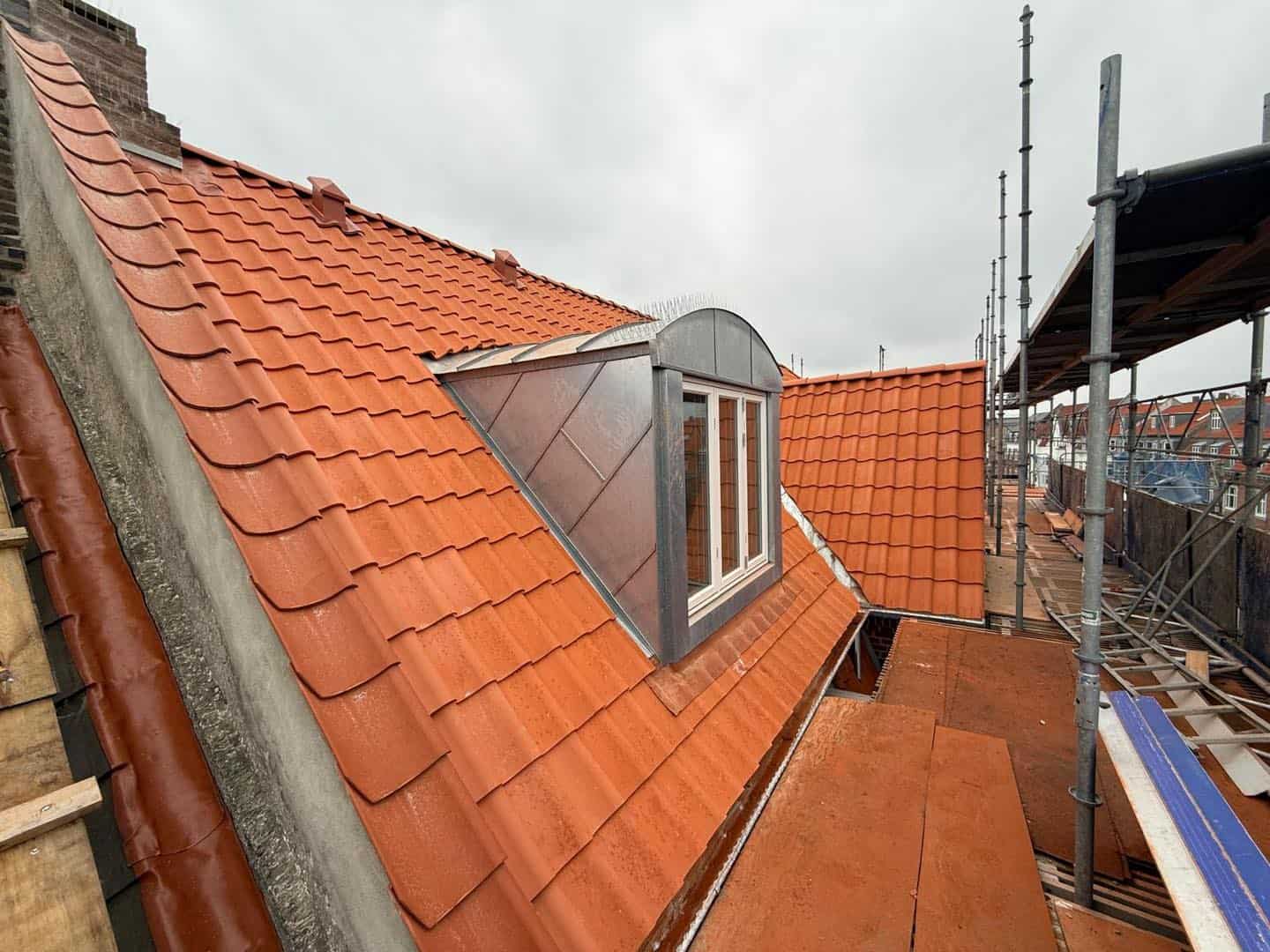 Tag på ejendom med nyt, rødt tegltag og tagvindue under renovering.