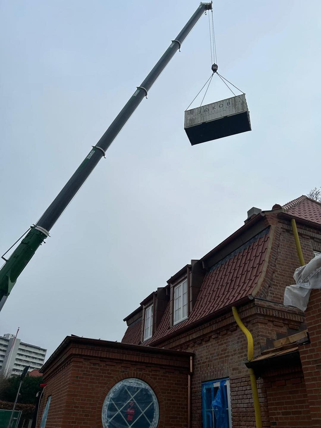 Kran løfter tungt byggemateriale til murstenshus under renovering eller opførelse.