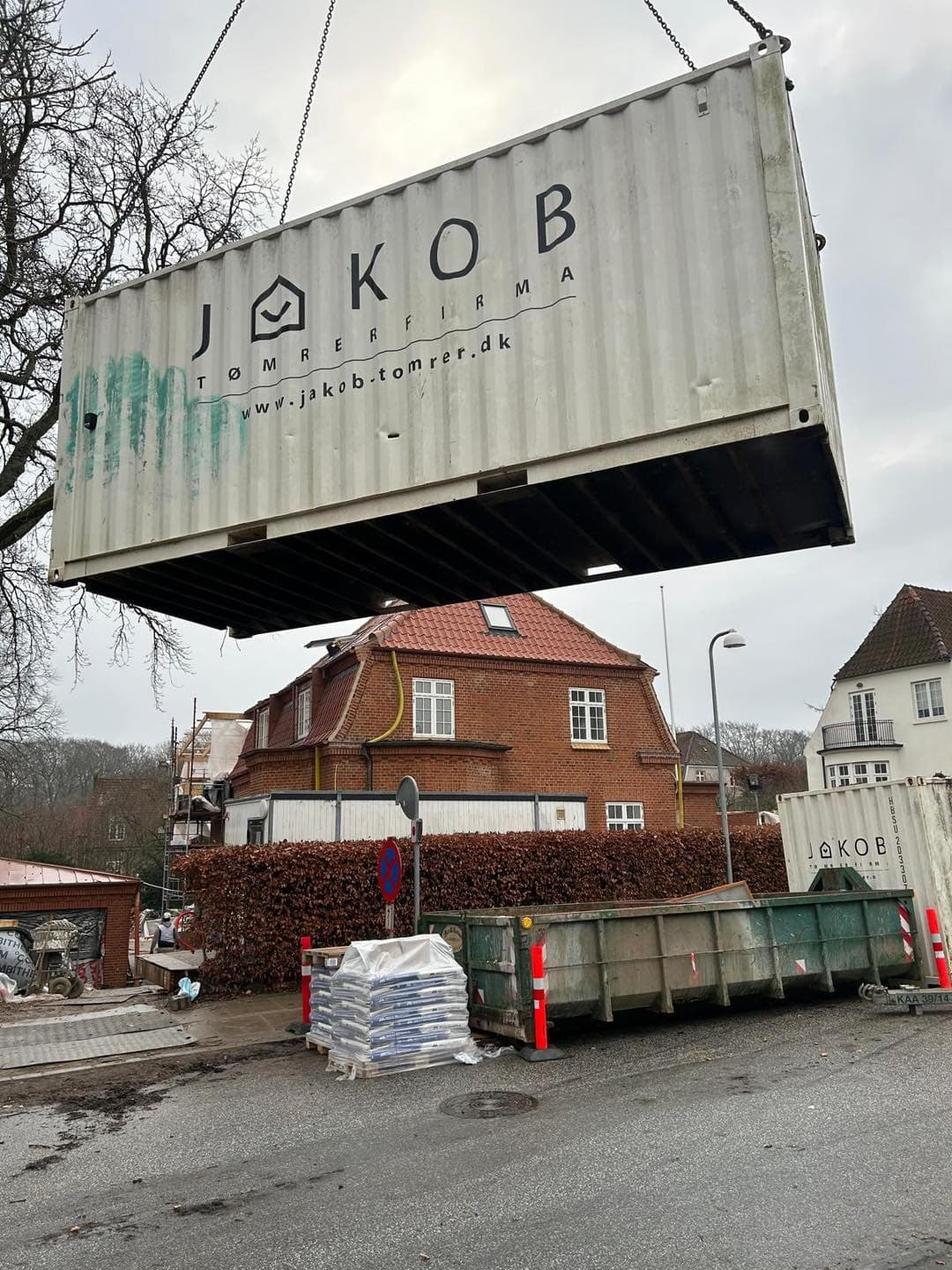 Skilt for Jakob Tømrerfirma A/S med logo og hjemmeside, monteret over byggeplads.