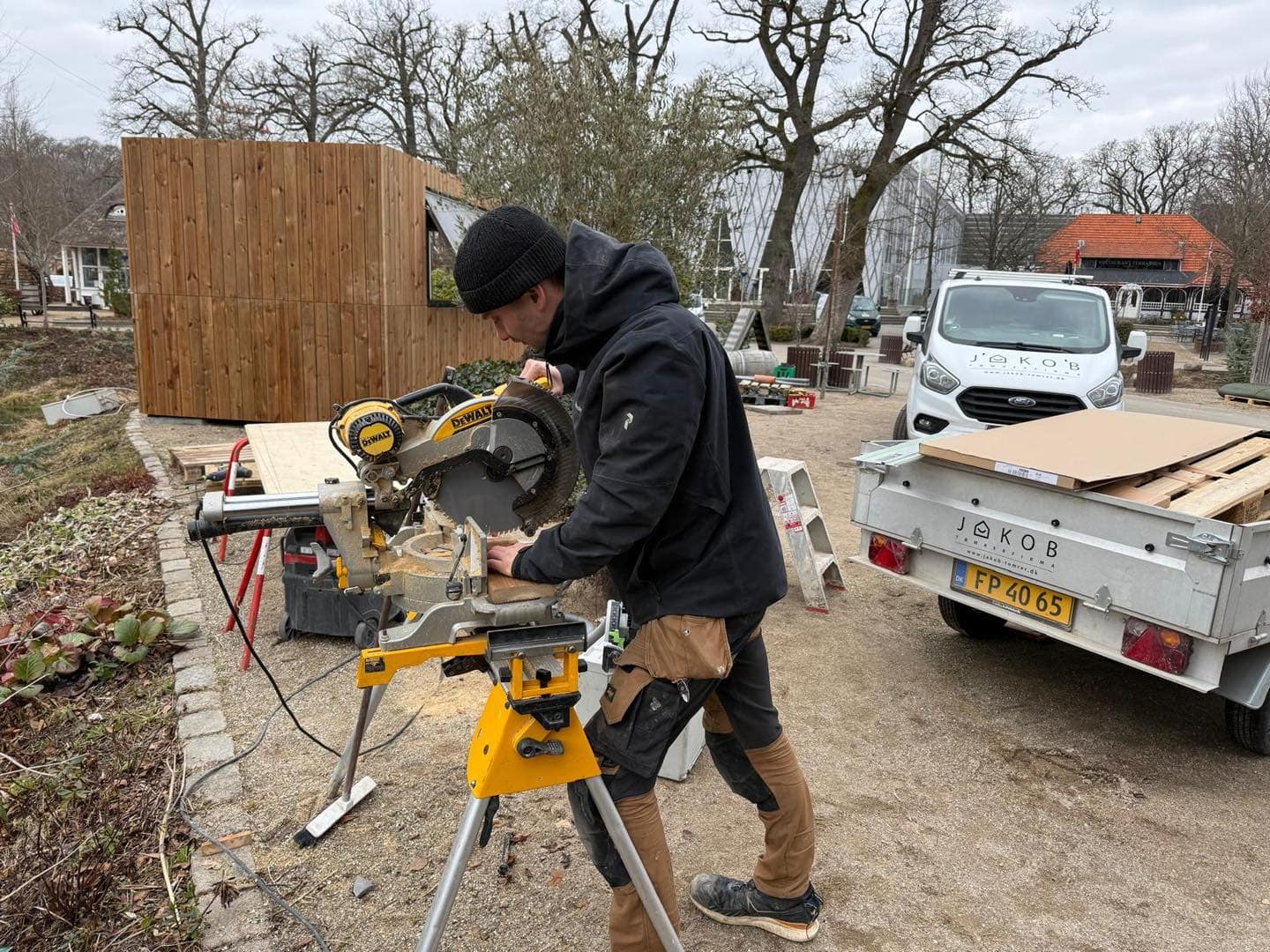 Tømrer arbejder med sav i udendørs byggeplads i Danmark.