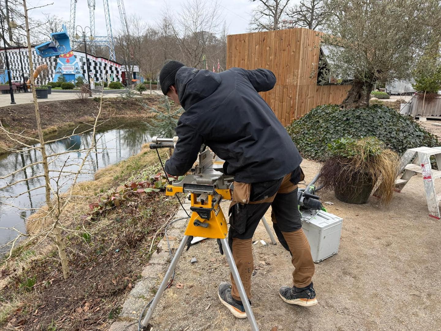 Tømrer måler og arbejder med værktøj udendørs ved byggeprojekt.