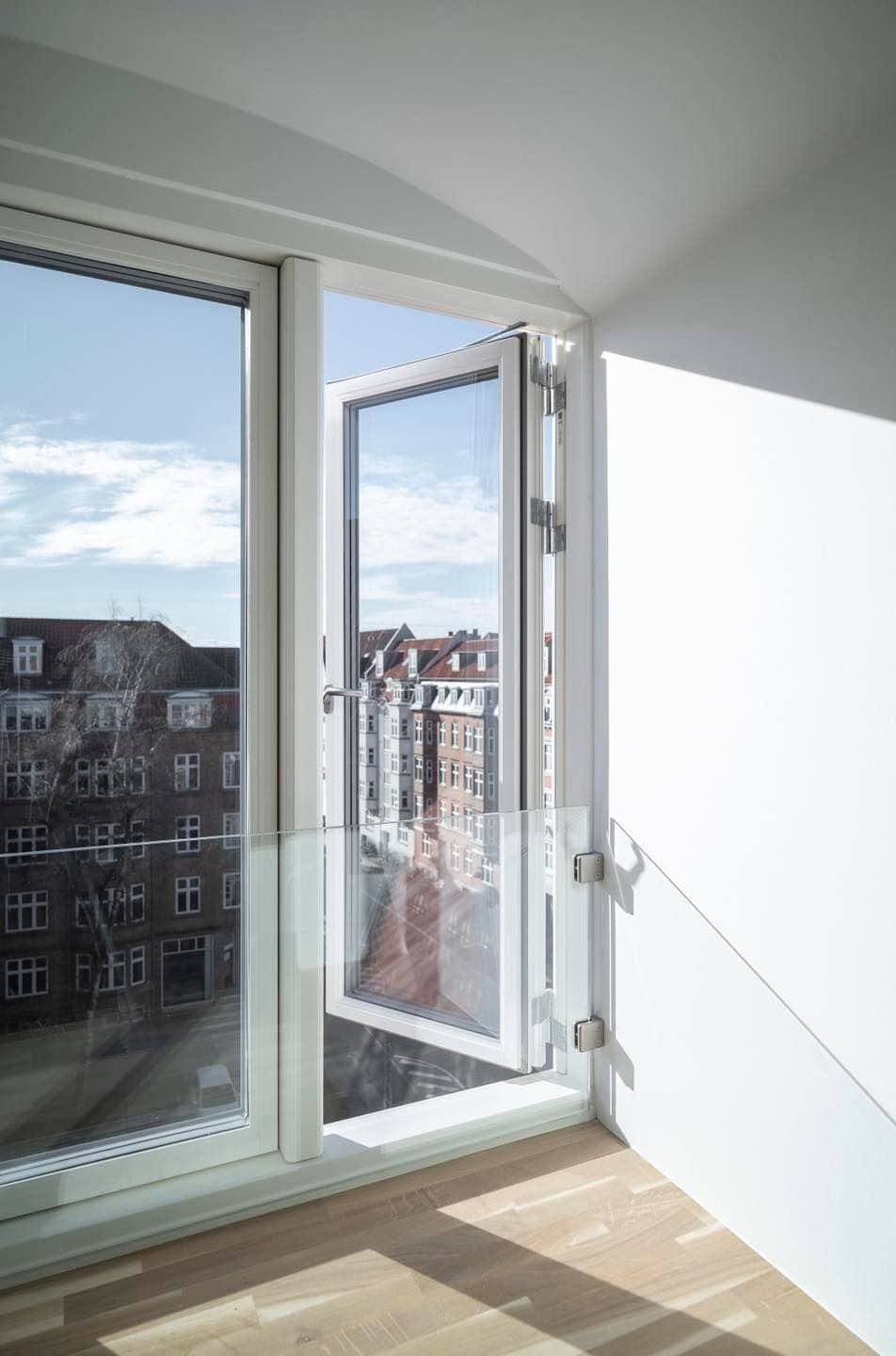 Åben altandør med udsigt over byen og blå himmel.