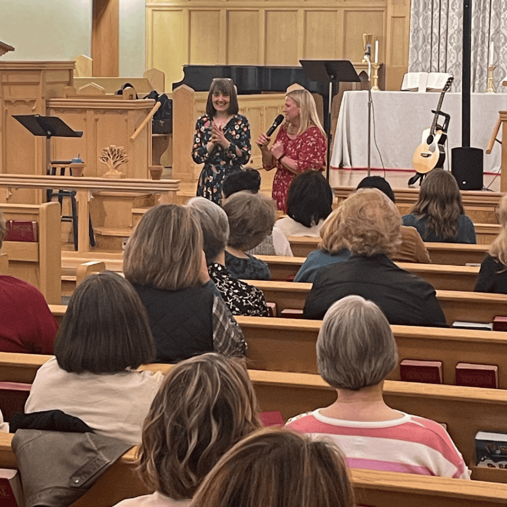 Women speaking at church event with audience listening attentively.