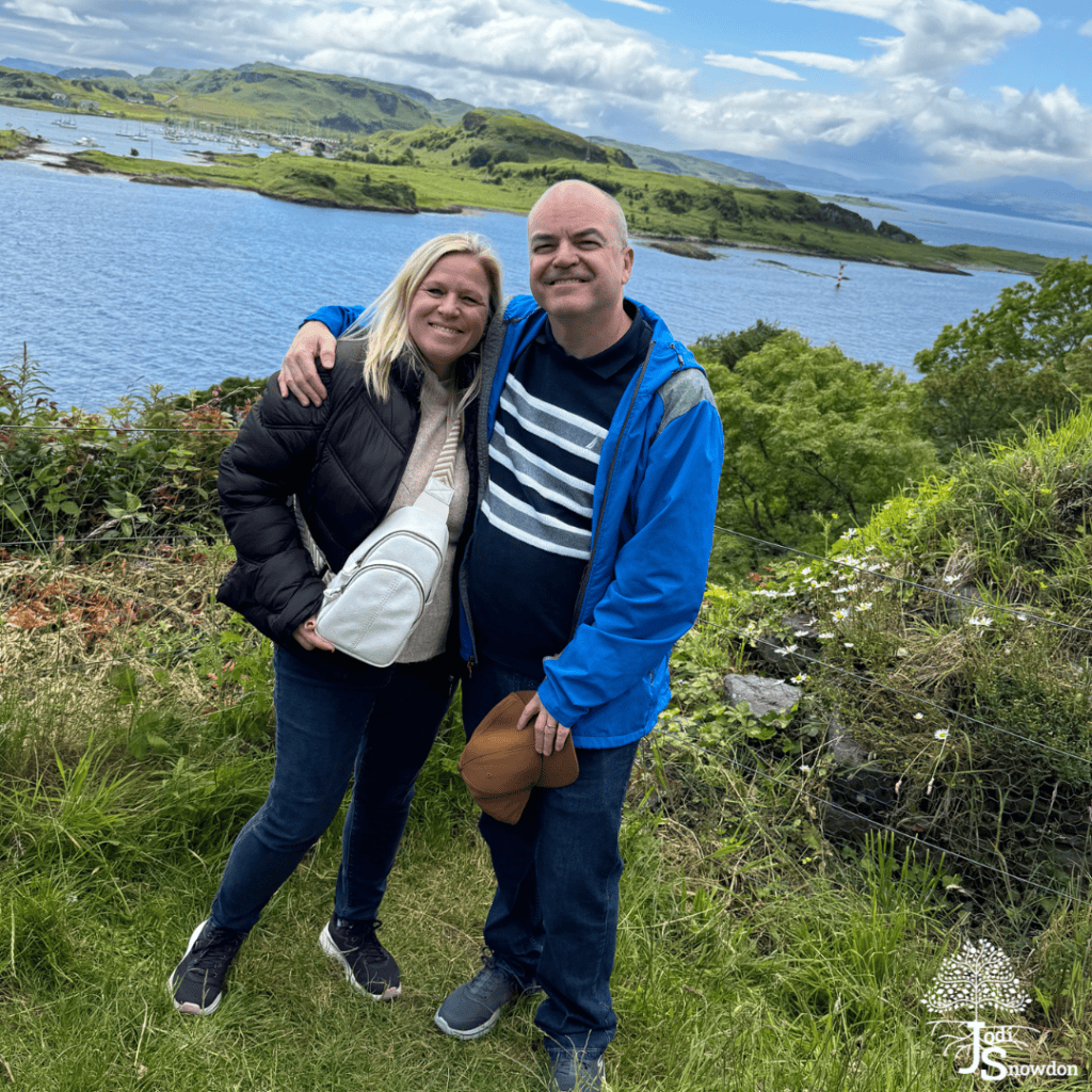 Happy couple enjoying scenic Scottish landscape by a lake with hills and clouds.