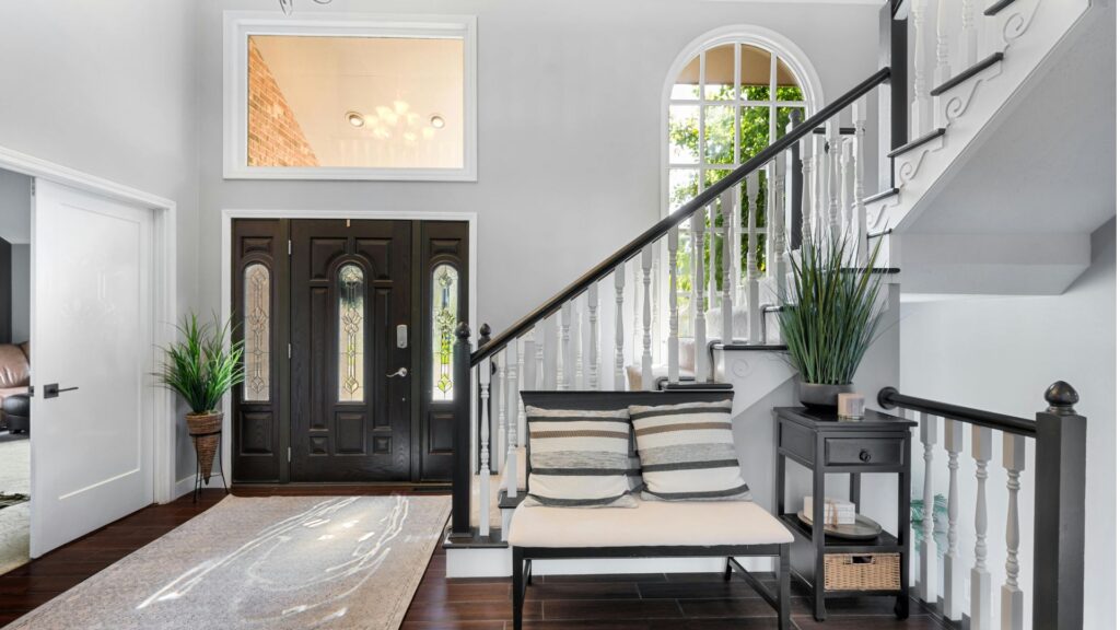 Interior view of a stylish home entrance featuring a staircase, black front door, and lush green pla.