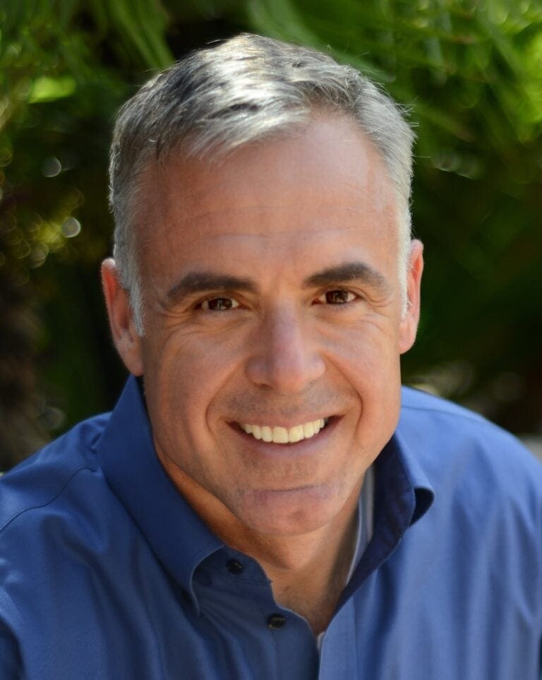 John Schloz smiling outdoors in a blue shirt.