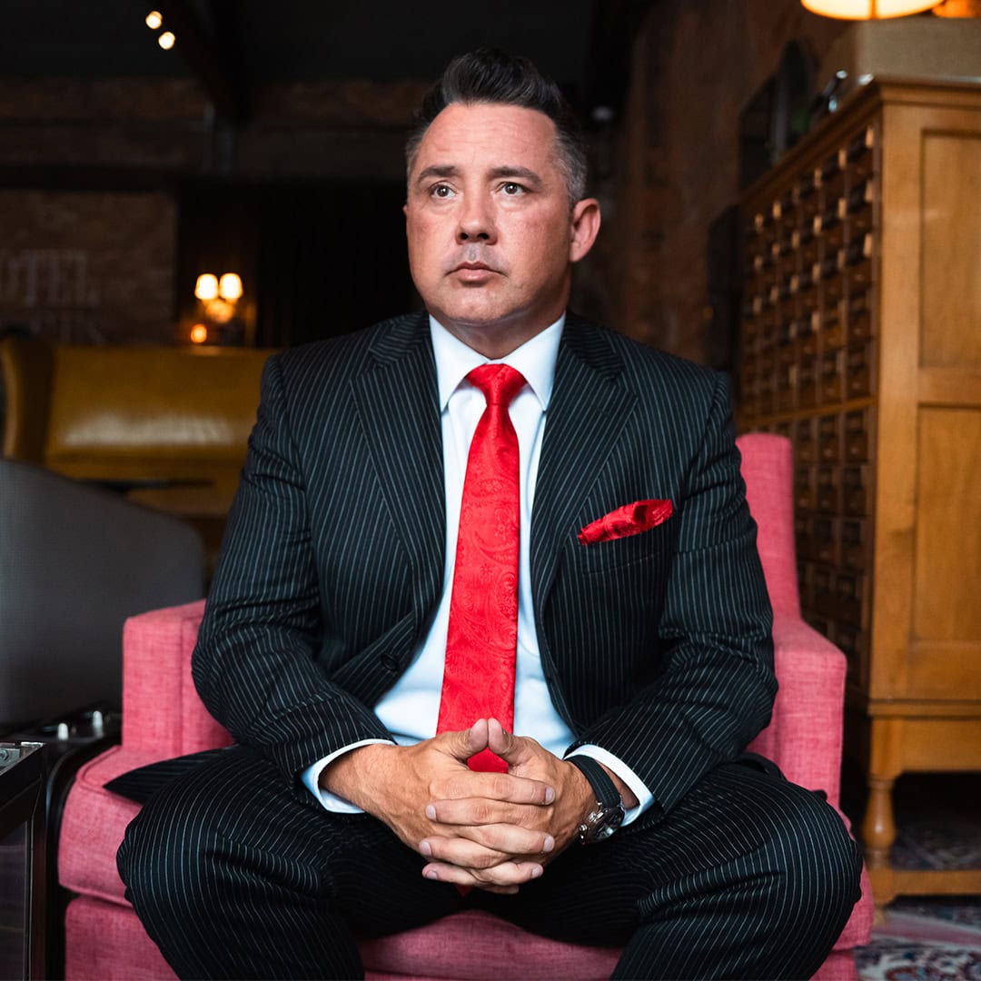 Professional businessman in a pinstripe suit with a red tie, sitting confidently in a stylish office space, representing leadership, branding, and marketing success.