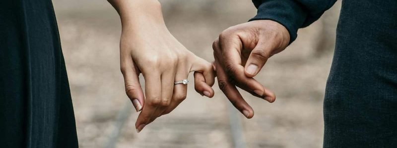 Close-up of a couple holding hands on train tracks, symbolizing connection and support.