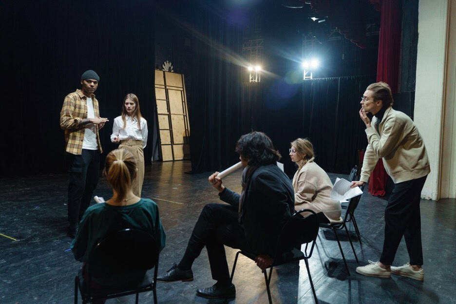Two adults on a stage with four adults sitting giving them feedback